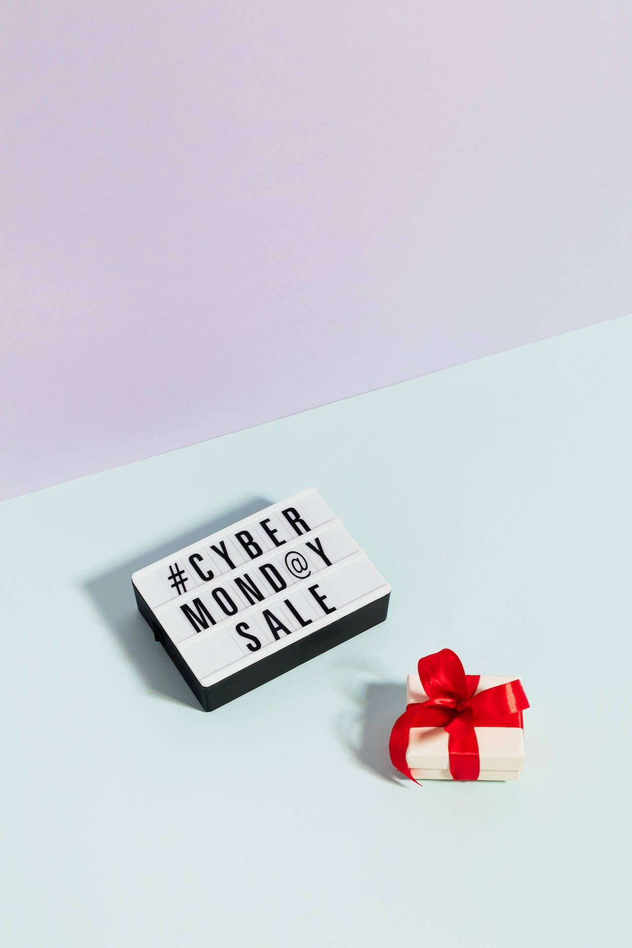 紅色動圖 桌布 壁紙 — 極簡風格的平鋪構圖，一個燈箱顯示 #CYBERMONDAY SALE，旁邊是一個繫著紅色蝴蝶結的小白色禮物盒，背景為雙色粉彩。
