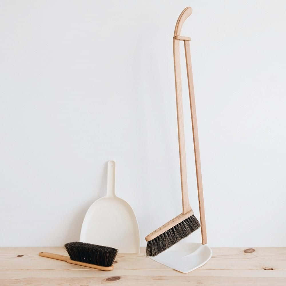 Broom 桌布 壁紙 — 極簡風格的木掃帚和簸箕套裝，帶黑色刷毛，放在淺色木地板上，背景是純白牆壁。