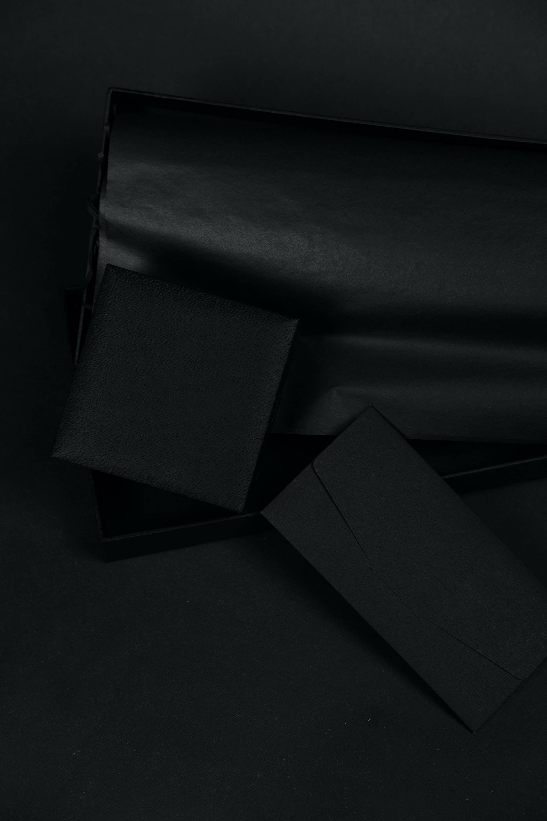 black aesthetic tumblr iPhone 桌布 壁紙 — 極簡黑色信封和盒子排列在深色表面上，帶有柔和陰影和細微紋理。