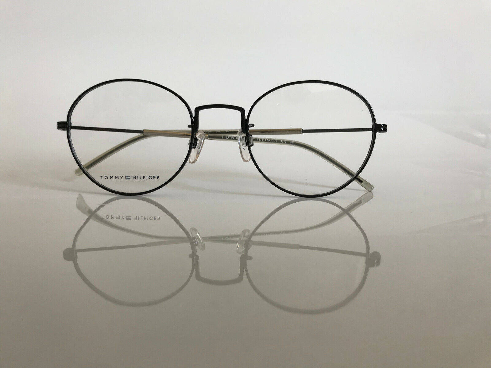 glasses 桌布 壁紙 — 極簡黑色圓框Tommy Hilfiger眼鏡放在反光的白色表面上，帶有清晰乾淨的陰影。