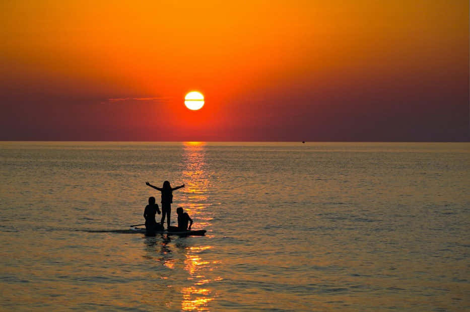 Lake Erie 桌布 壁紙 — 槳板上的剪影人物在平靜的海面上日落時張開雙臂。