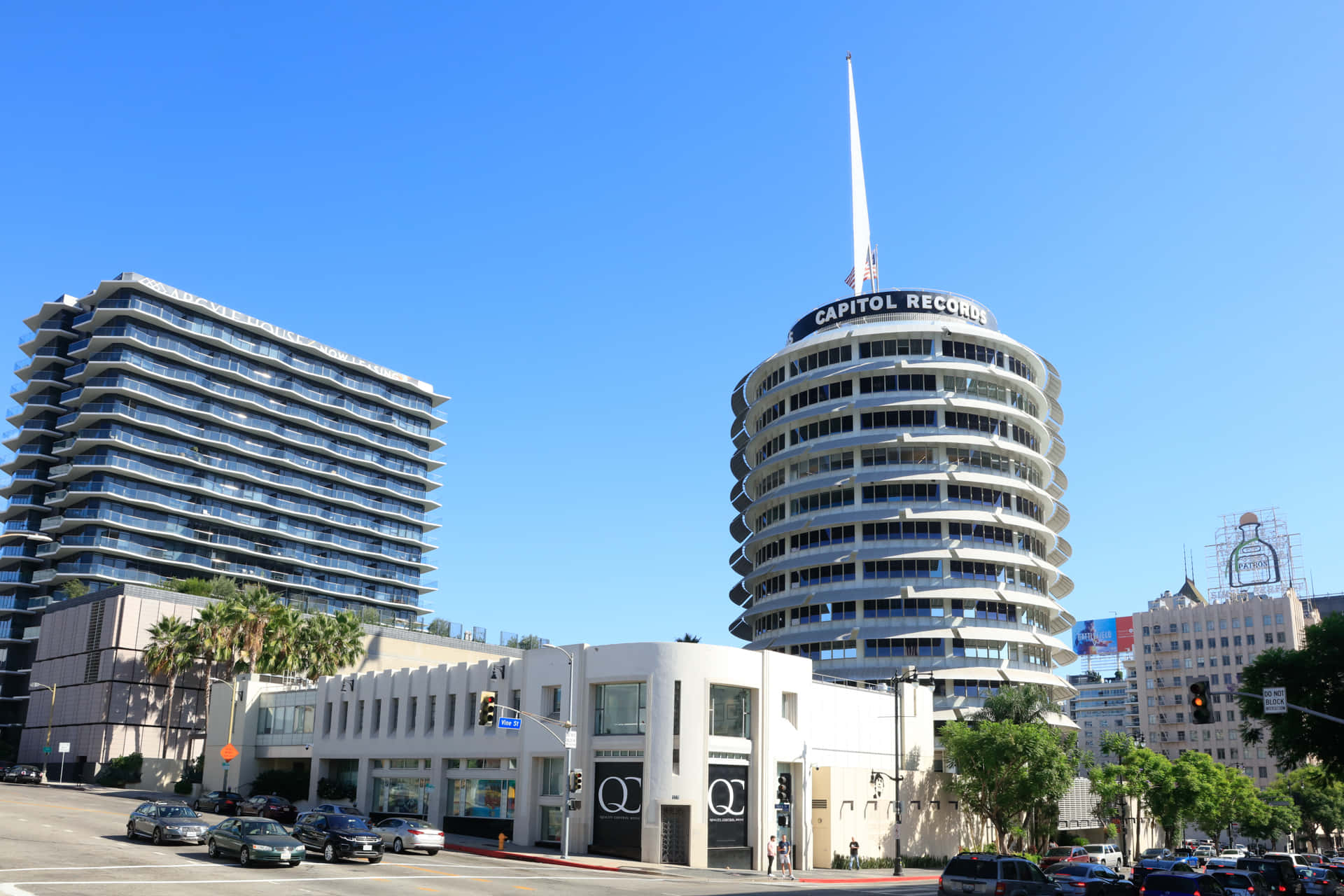 Buildings 桌布 壁紙 — 標誌性的 Capitol Records 大樓在晴朗的藍天下高聳矗立，現代化的玻璃塔樓和棕櫚樹排列在下方繁忙的街道兩旁。