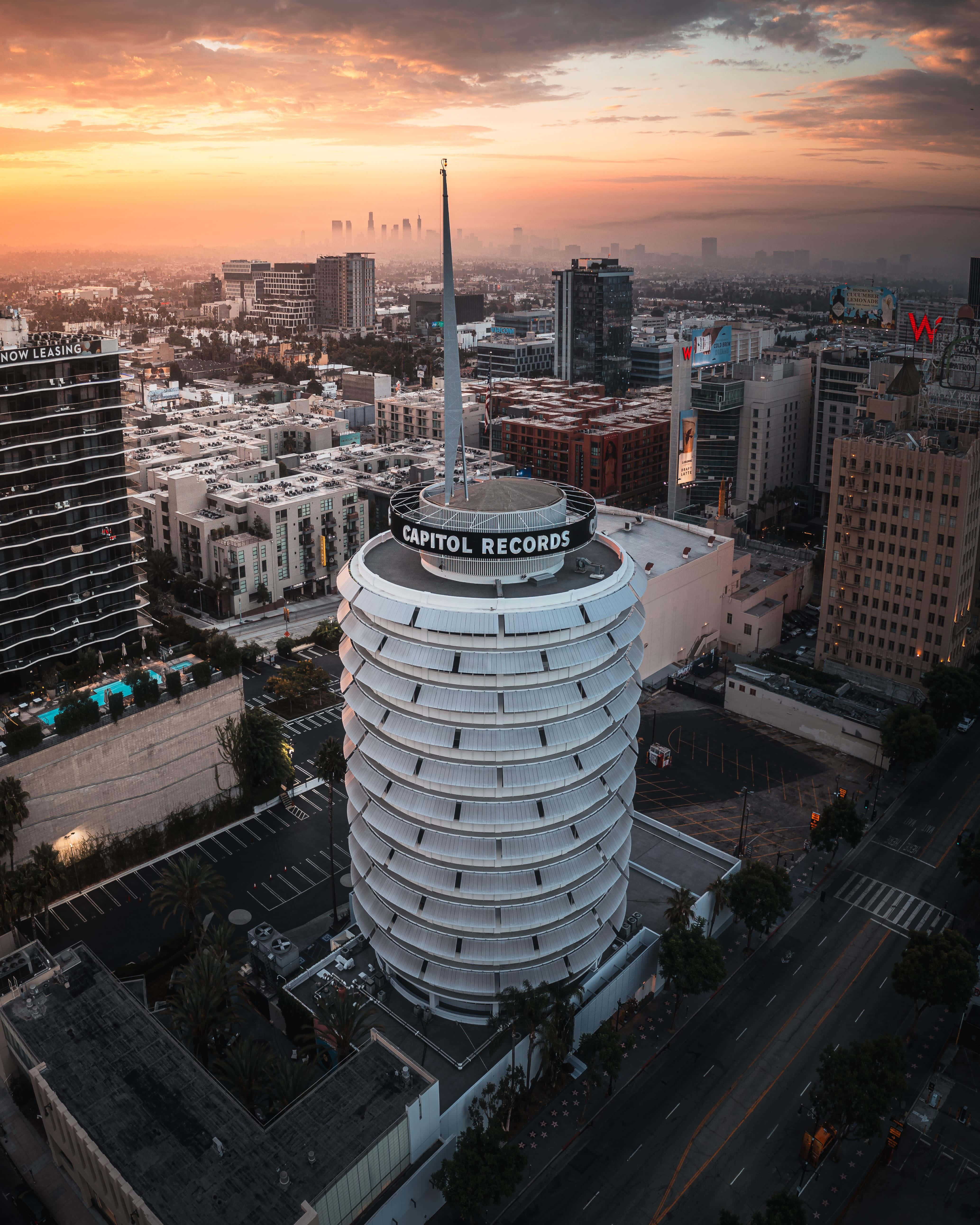 太陽 桌布 壁紙 — 標誌性的 Capitol Records 大樓在日落時的鳥瞰圖，溫暖的橙色天空和下方的城市景觀。
