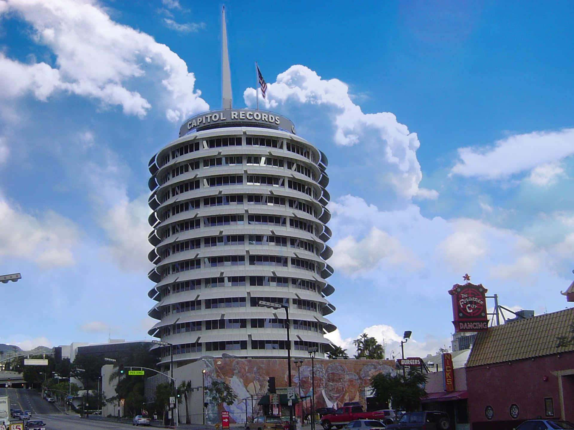 雲朵 桌布 壁紙 — 標誌性的 Capitol Records 大樓在晴朗的藍天和白雲下高聳，周圍是城市街道和復古標誌。