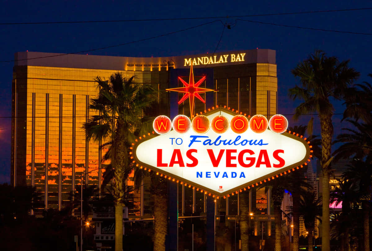 Nevada 桌布 壁紙 — 標誌性的拉斯維加斯歡迎標誌在夜間閃耀，棕櫚樹和曼德勒海灣酒店在後面。