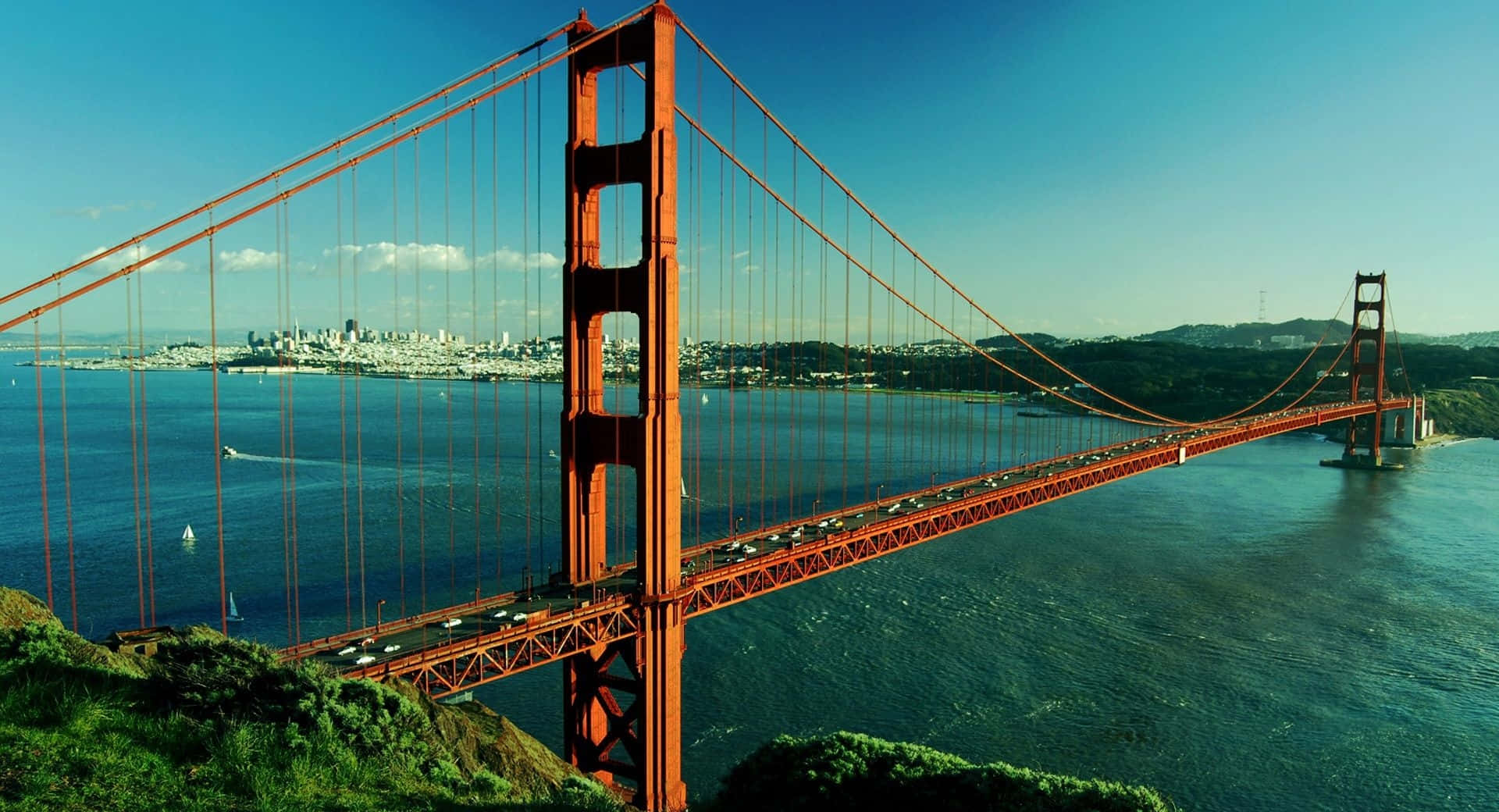 bridge 桌布 壁紙 — 標誌性的橙色金門大橋橫跨深藍色海灣，天空晴朗，遠處是舊金山天際線。