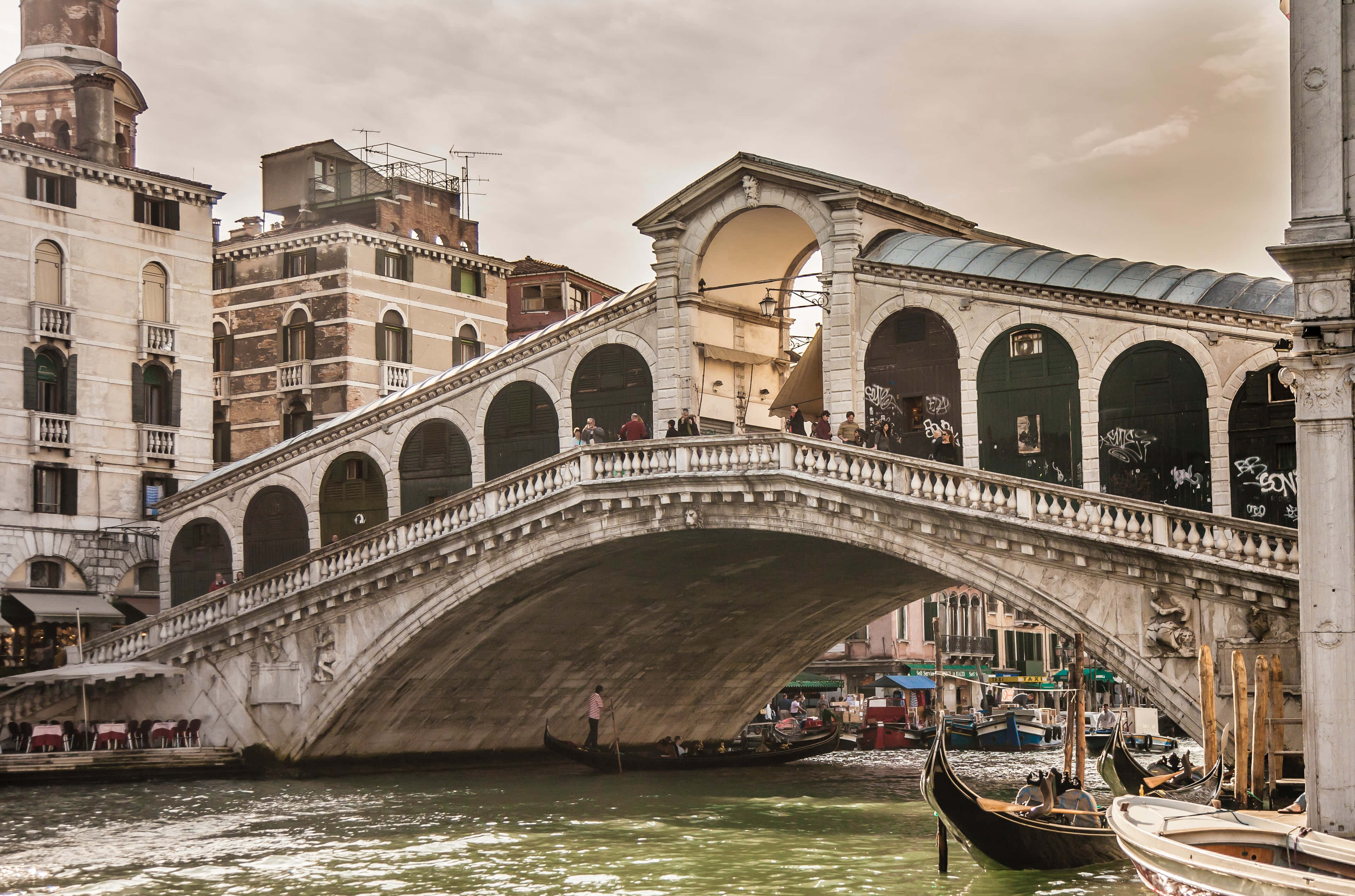 venice 桌布 壁紙 — 標誌性的石橋嘆息橋在陰天下，與貢多拉和歷史建築一起拱跨威尼斯運河。