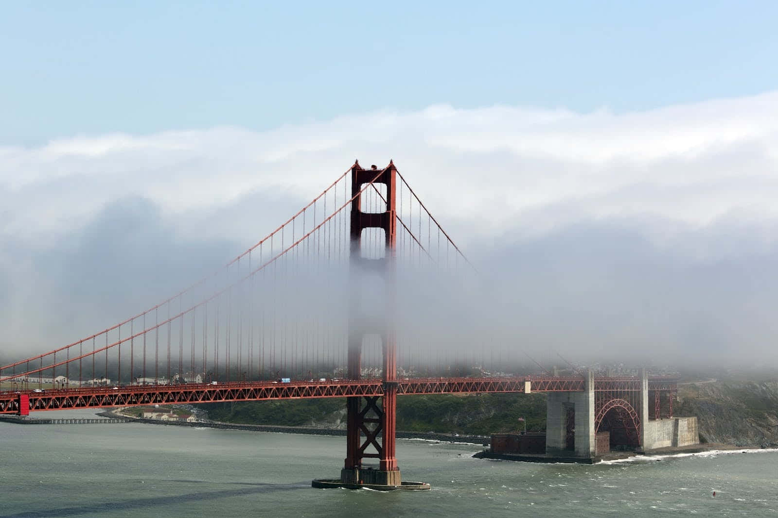 San Francisco Fog 桌布 壁紙 — 標誌性的紅色金門大橋從海岸霧中浮現，在淡藍色的天空下，霧氣在其塔樓周圍旋轉。