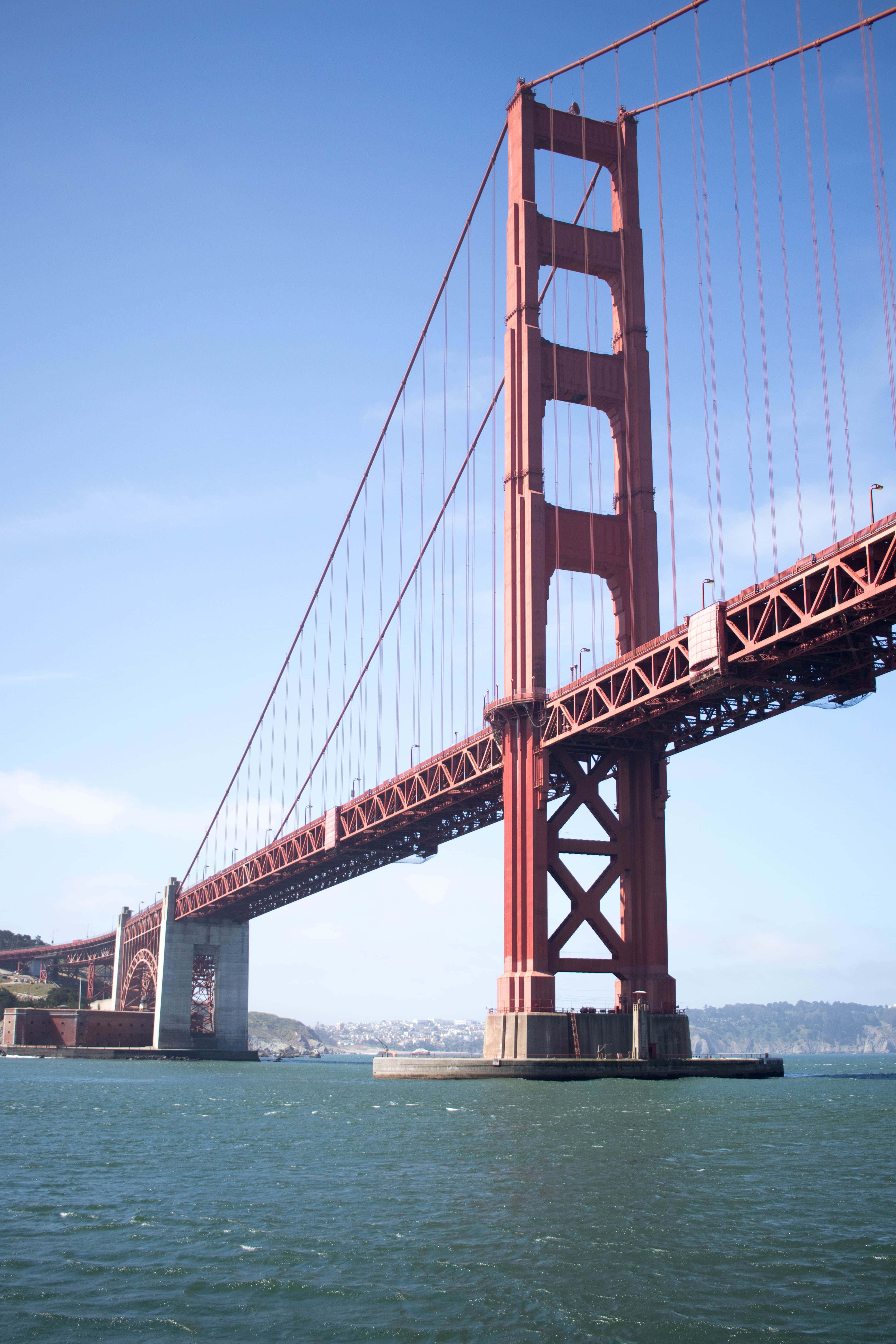 bridge 桌布 壁紙 — 標誌性的紅色金門大橋橫跨藍綠色的海灣，天空晴朗，遠處有山丘。