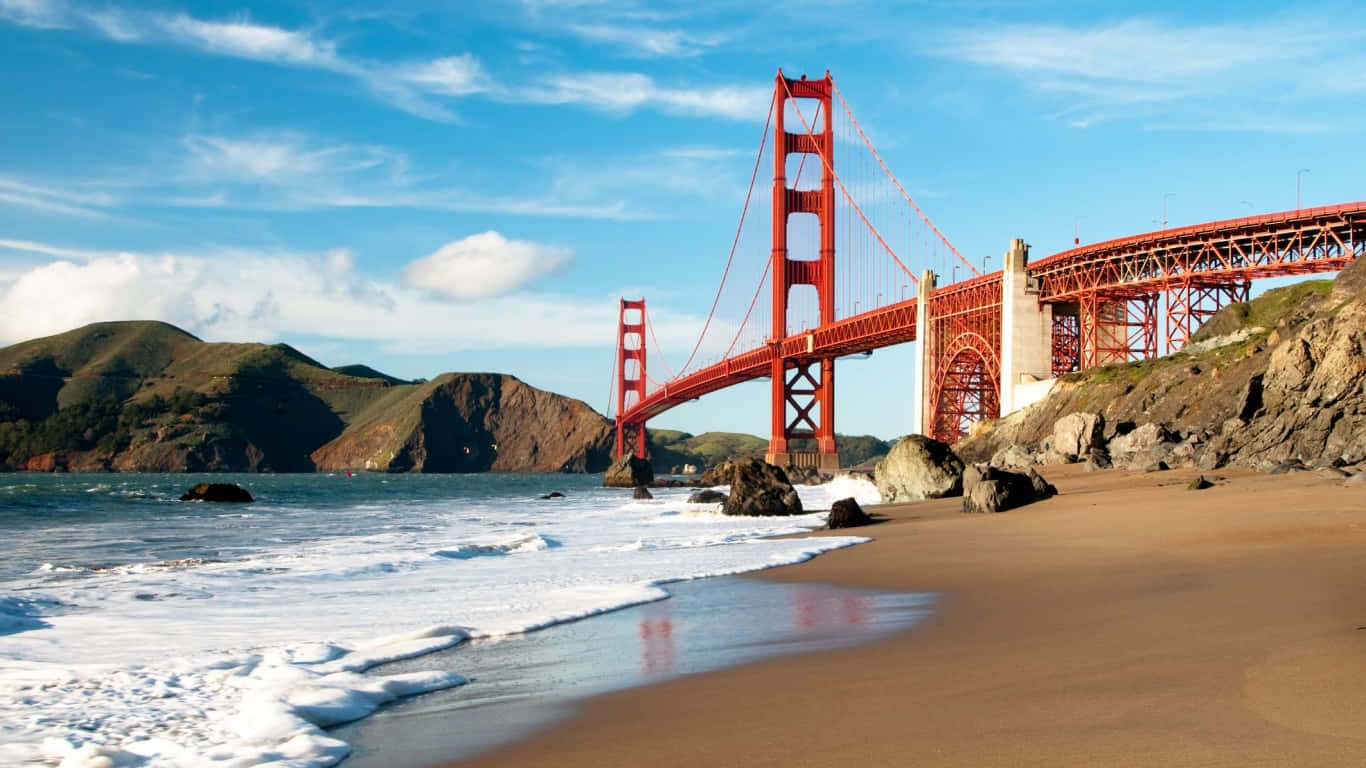 1366x768 San Francisco 桌布 壁紙 — 標誌性的紅色金門大橋橫跨藍色海灣，白浪拍打沙灘，天空部分多雲。
