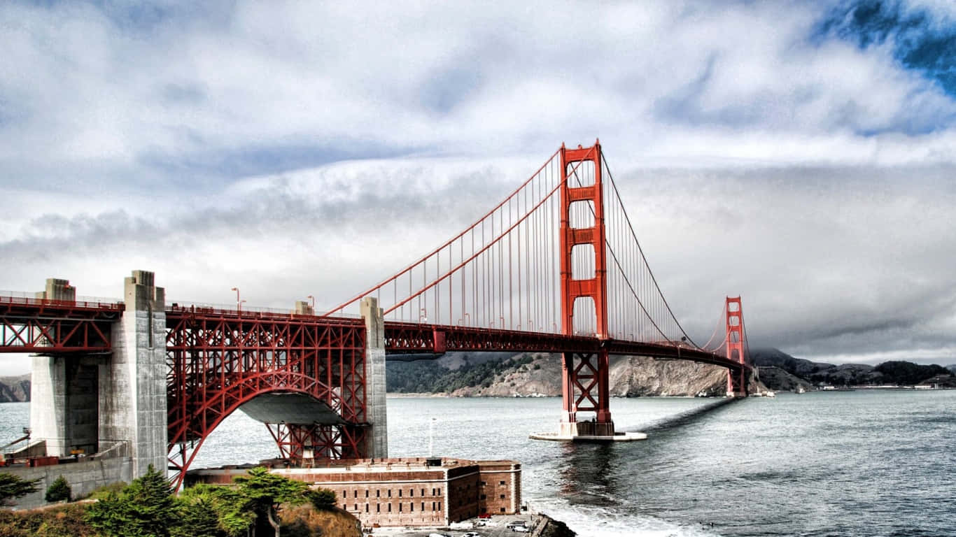 1366x768 San Francisco 桌布 壁紙 — 標誌性的紅色金門大橋橫跨迷霧籠罩的海灣，天空多雲，附近可見惡魔島。