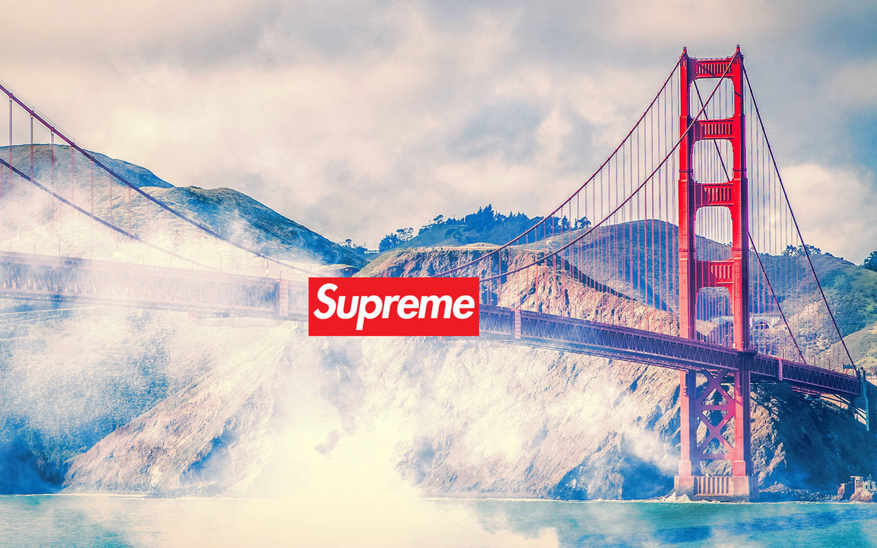 超屌 Supreme 桌布 壁紙 — 標誌性的金門大橋在霧氣繚繞的山丘前傲然聳立，場景上疊加了一個紅色的Supreme標誌。