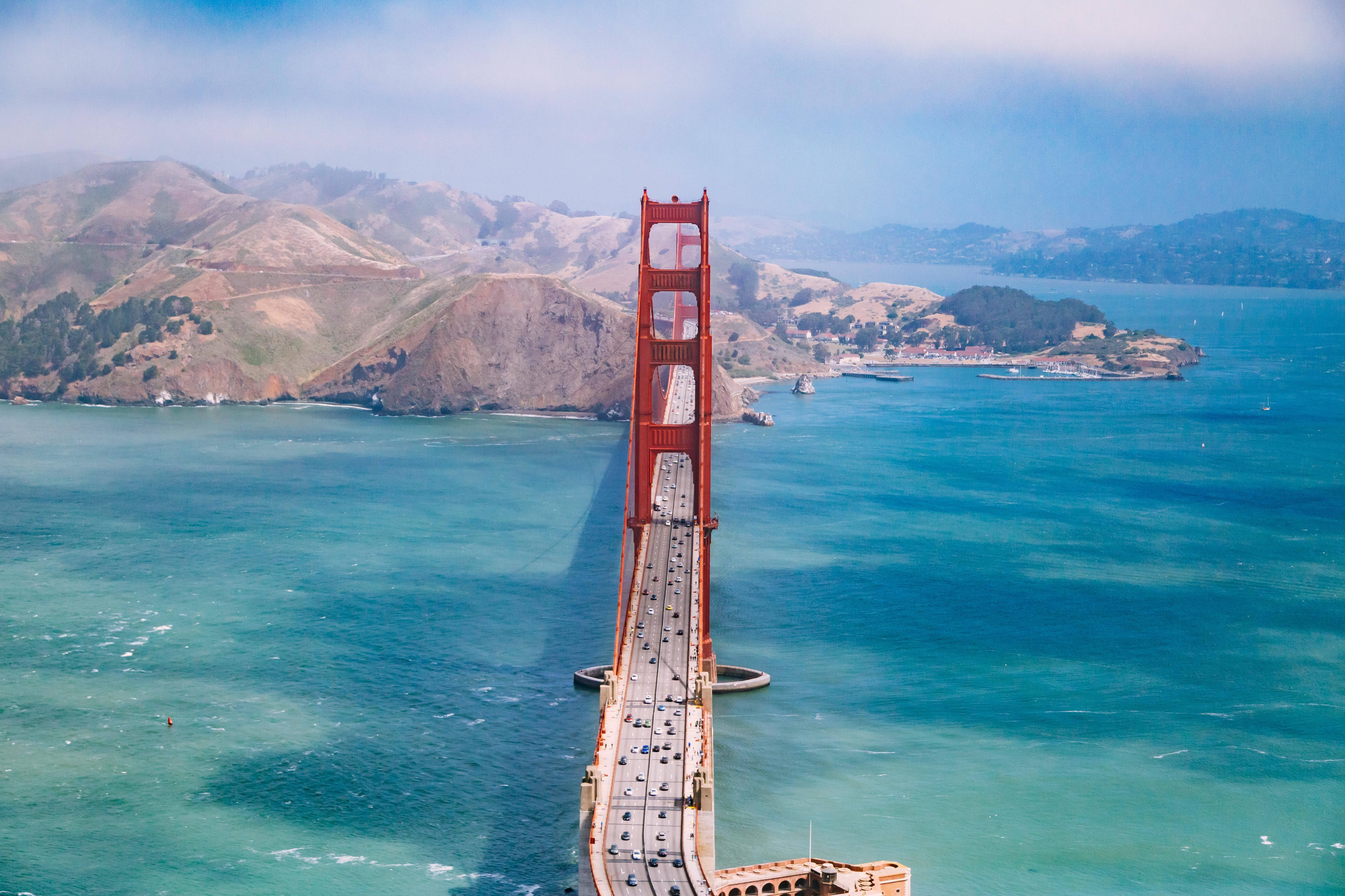 San Francisco Phone 桌布 壁紙 — 標誌性紅色金門大橋橫跨碧綠海水的空拍視角，背景有朦朧山丘。