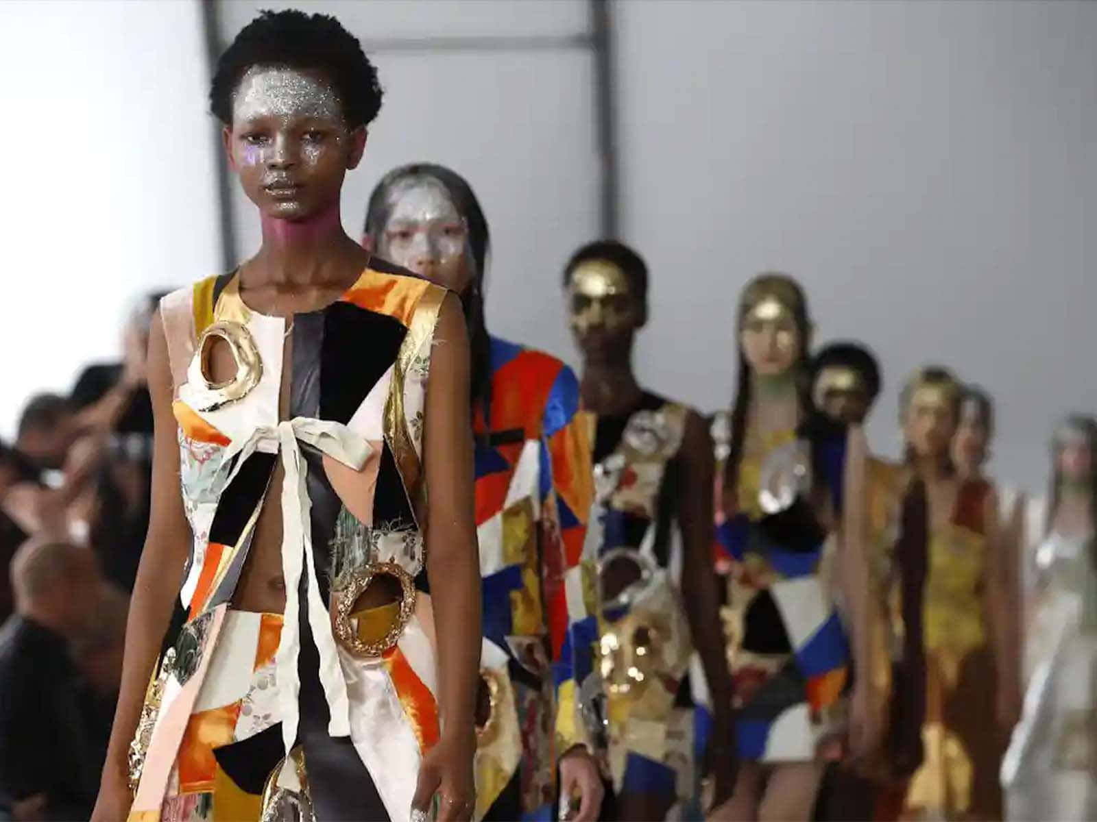 Runway 桌布 壁紙 — 模特兒在明亮燈光下，穿著前衛拼布服裝和金屬臉部彩繪走秀。