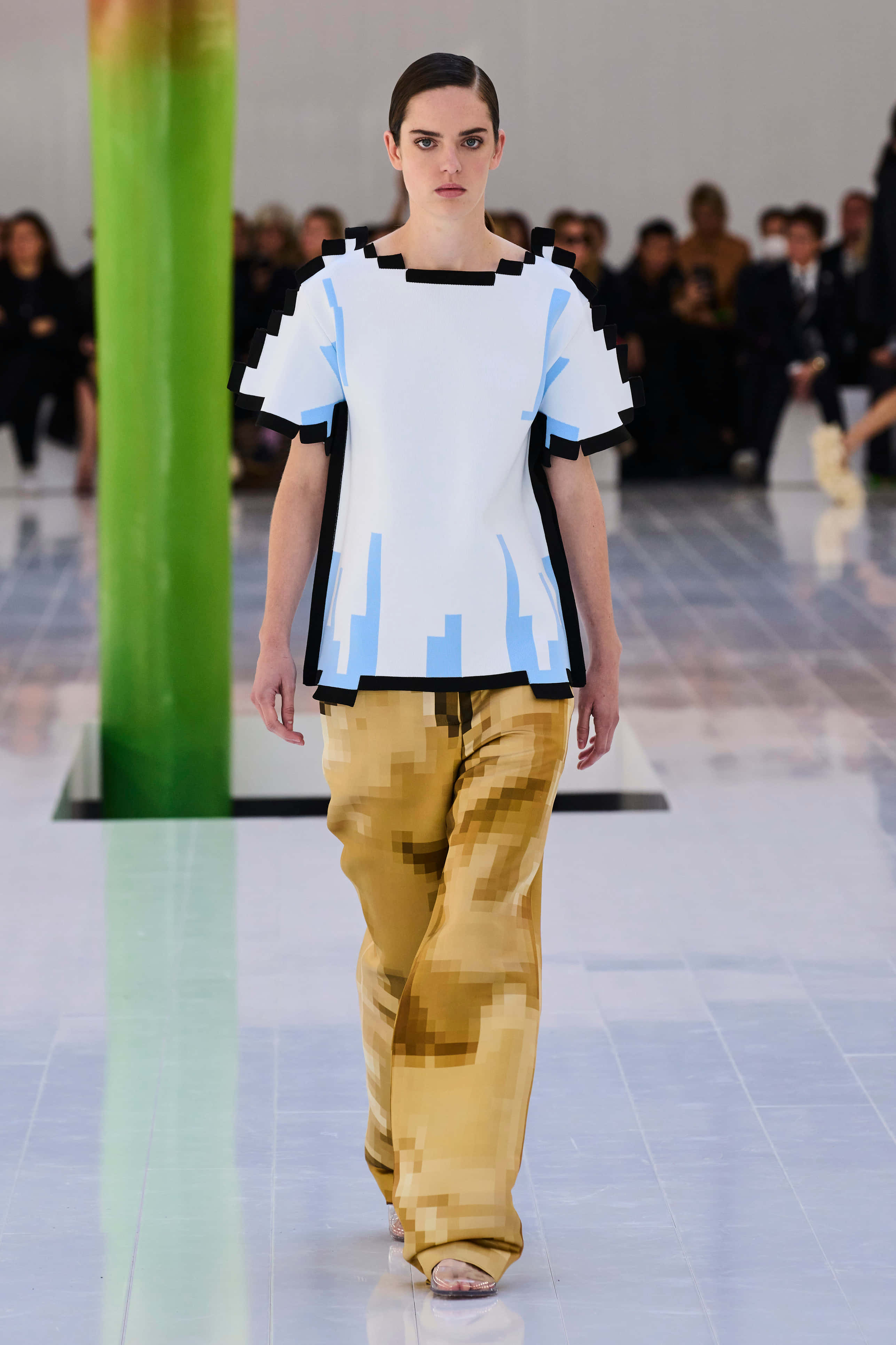 Runway 桌布 壁紙 — 模特兒在時裝伸展台上行走，身穿像素化藍白上衣和金色像素長褲，在明亮的攝影棚燈光下。