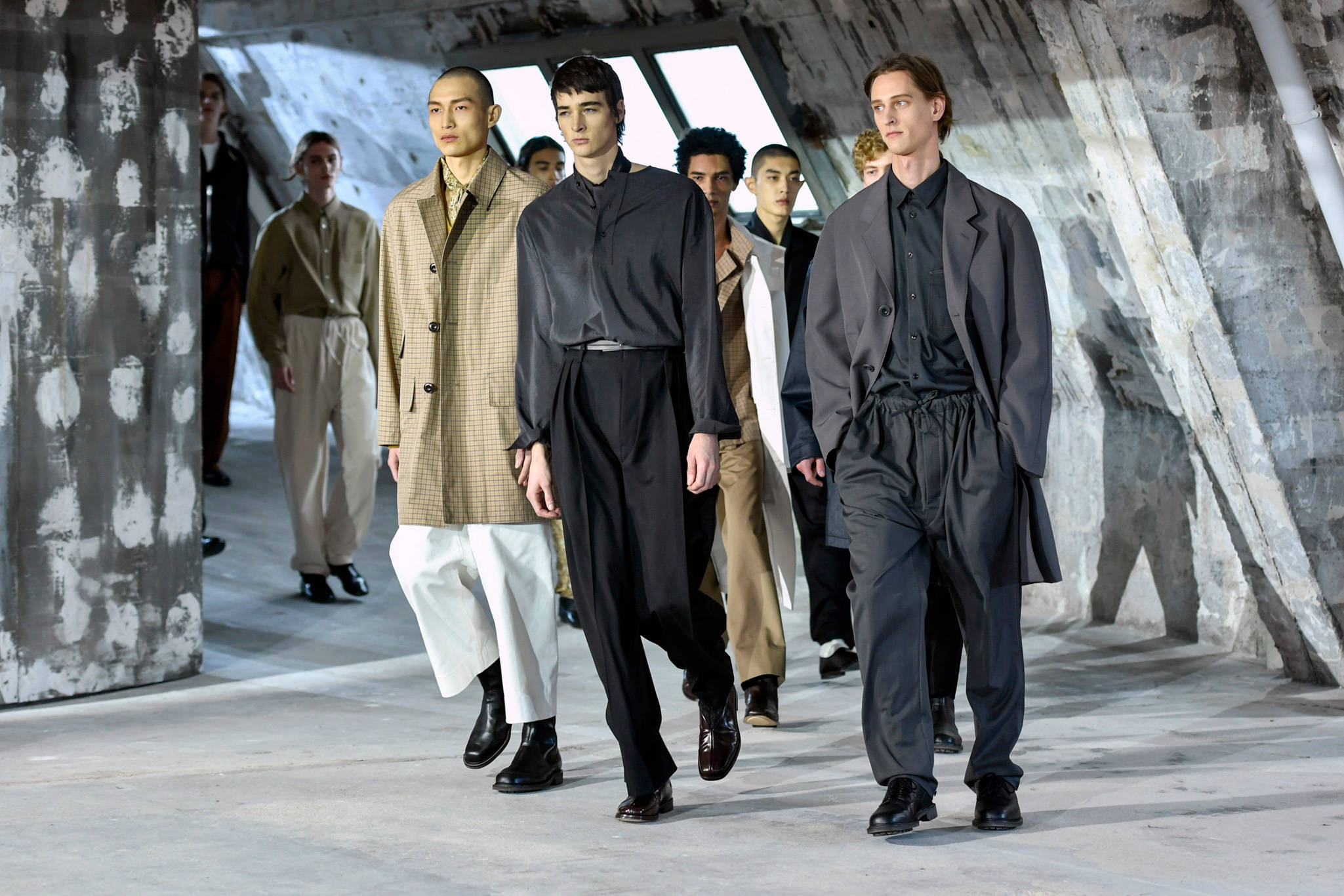 Mens Fashion 桌布 壁紙 — 模特兒在極簡時裝秀上，自信地在有角天窗下的混凝土天橋上行走。