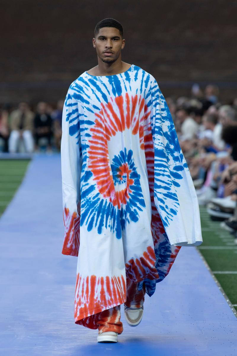 Fashion Model 桌布 壁紙 — 模特兒自信地走在藍色伸展台上，身穿搶眼的紅、藍、白紮染長袍，在明亮燈光下。