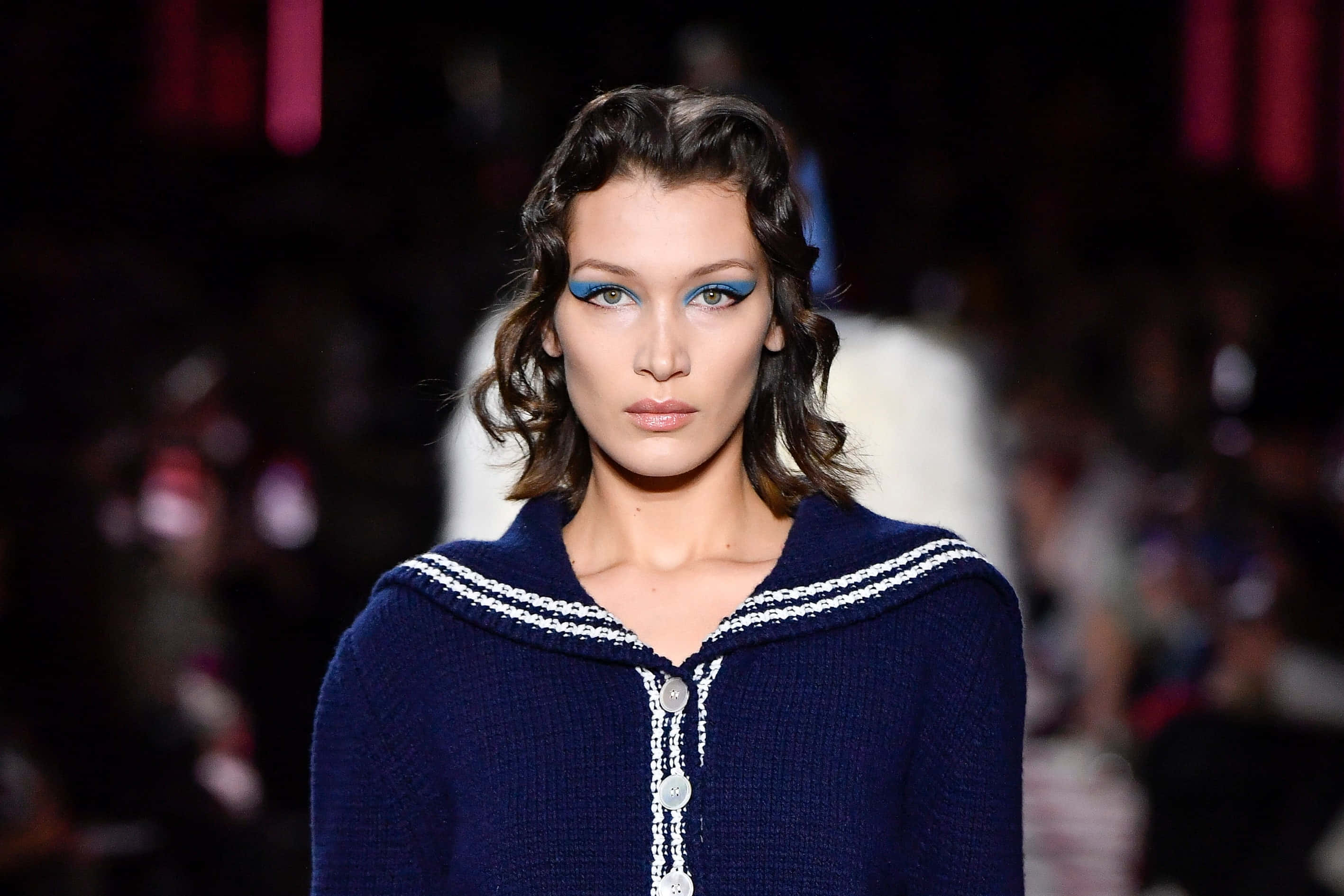 Fashion Model 桌布 壁紙 — 模特兒身穿海軍藍水手風格針織毛衣，搭配大膽的藍色眼線，在戲劇性的舞台燈光下走秀。