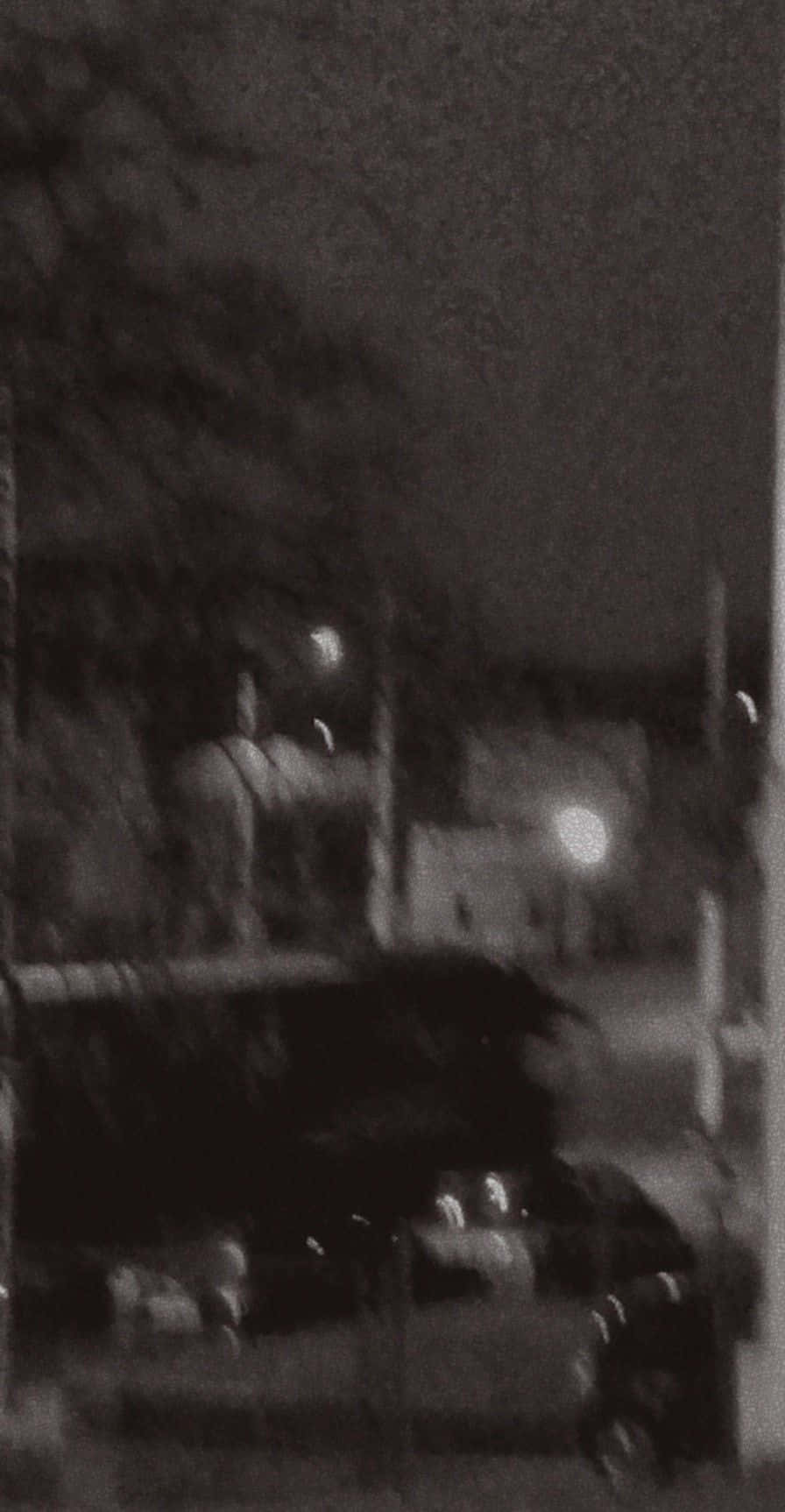 黑白 桌布 壁紙 — 模糊的夜晚街景，一輛深色汽車和遠處發光的燈光，在柔和的天空下。