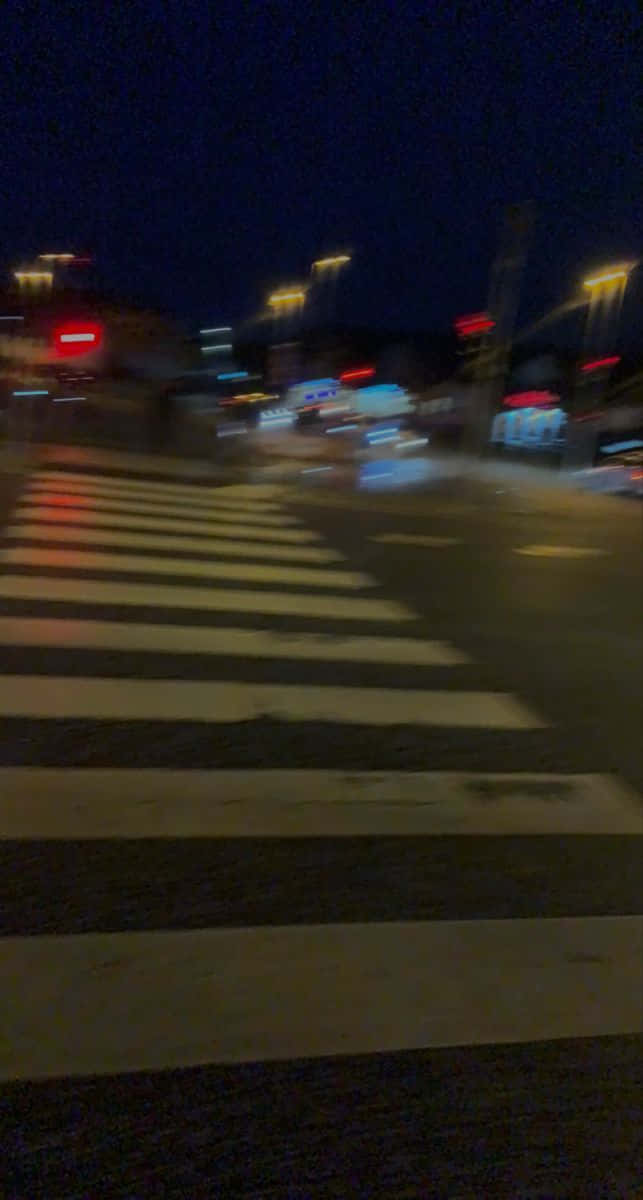 Road 桌布 壁紙 — 模糊的夜晚街景，車燈在路燈下的斑馬線上劃過光軌。