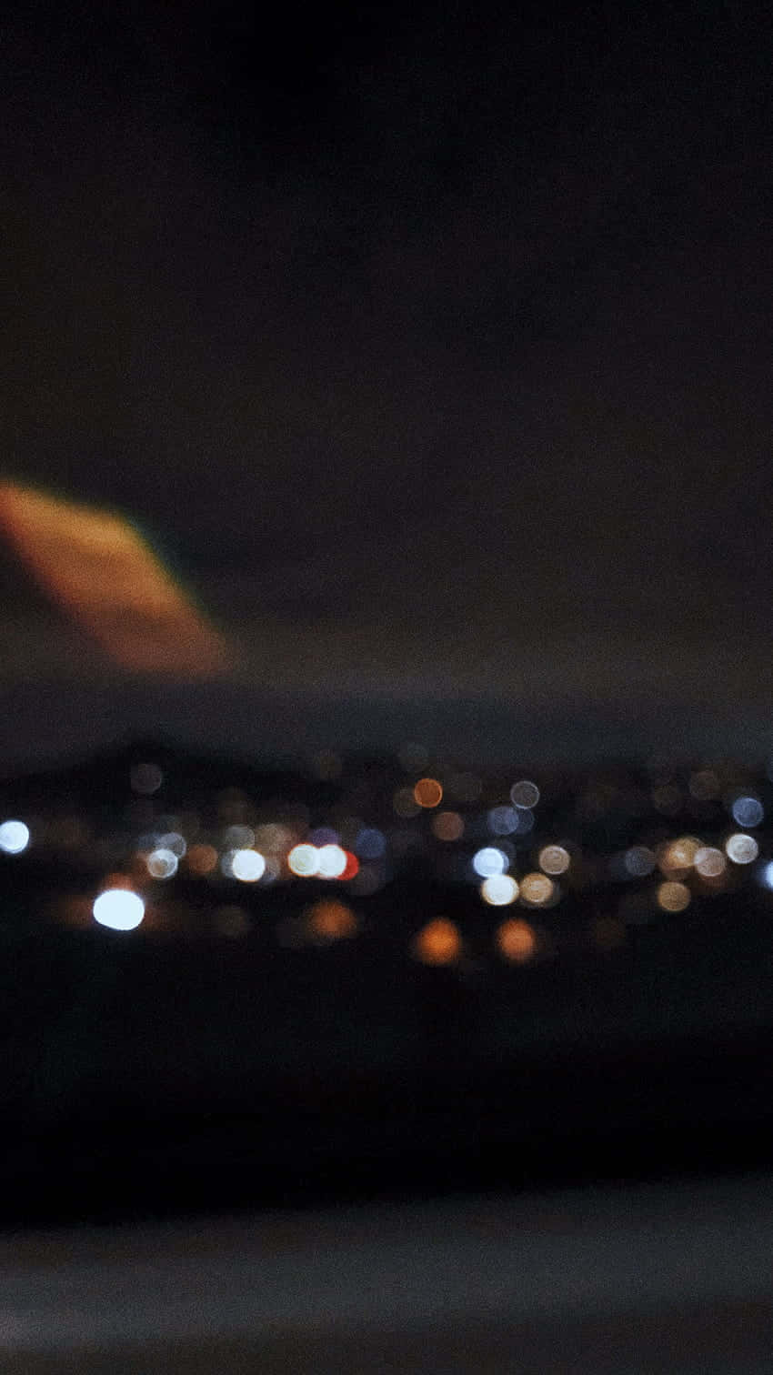 Black Blur 桌布 壁紙 — 模糊的夜景城市景觀，帶有發光的散景燈光和天空中溫暖的橙色條紋。