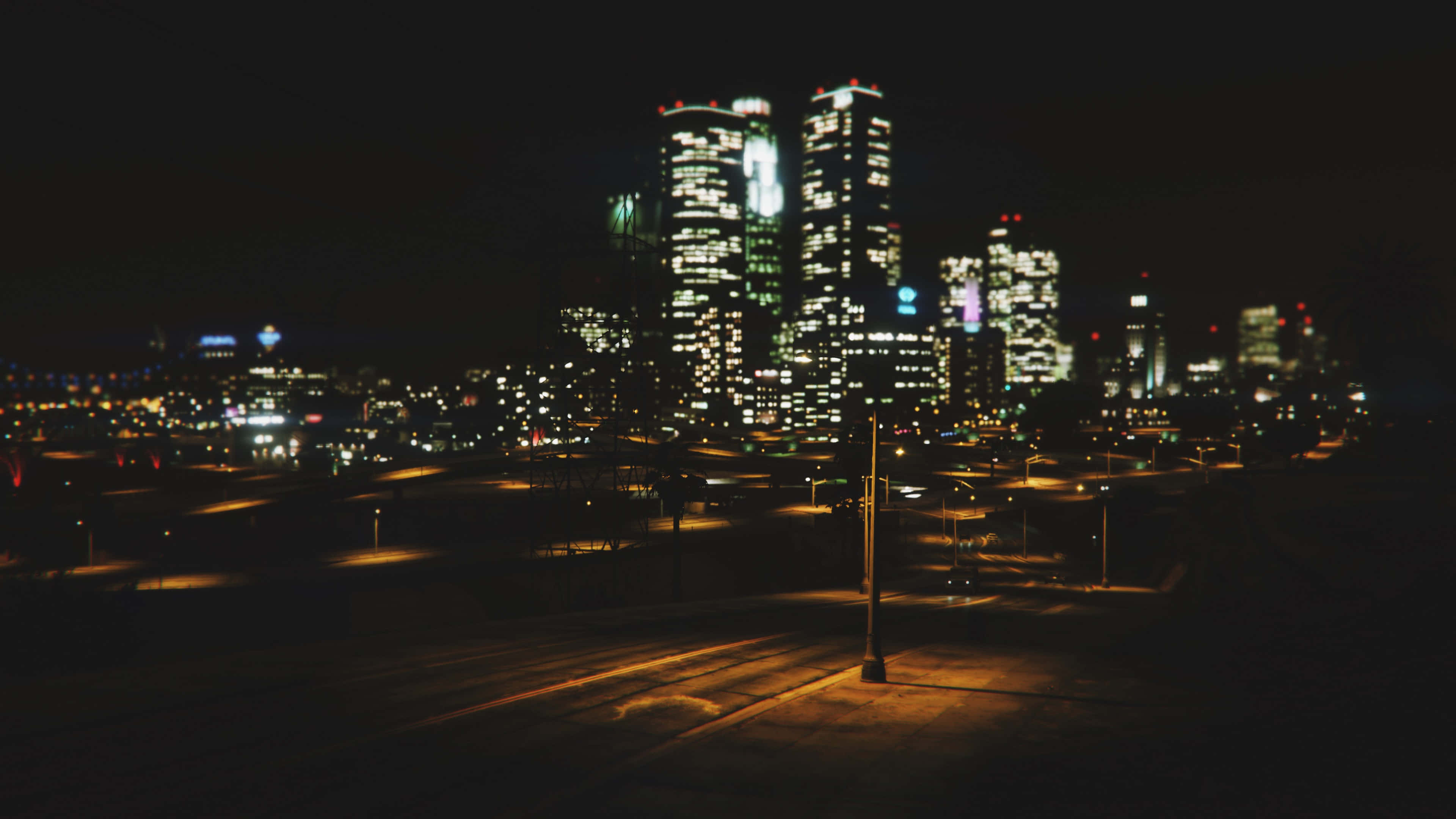 風景 桌布 壁紙 — 模糊的夜景城市景觀，閃爍的摩天大樓和溫暖的路燈在空曠的道路上投下長長的陰影。