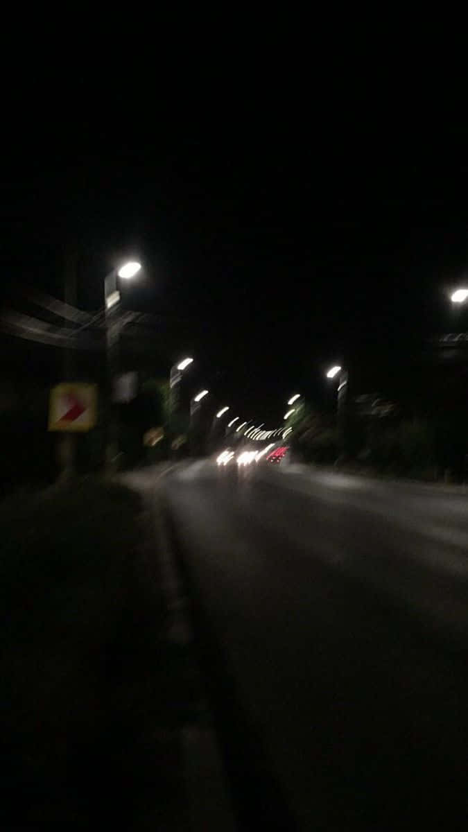 Street Light 桌布 壁紙 — 模糊的夜間駕駛，沿著一條昏暗的街道，街燈和遠處的車頭燈刺破黑暗。