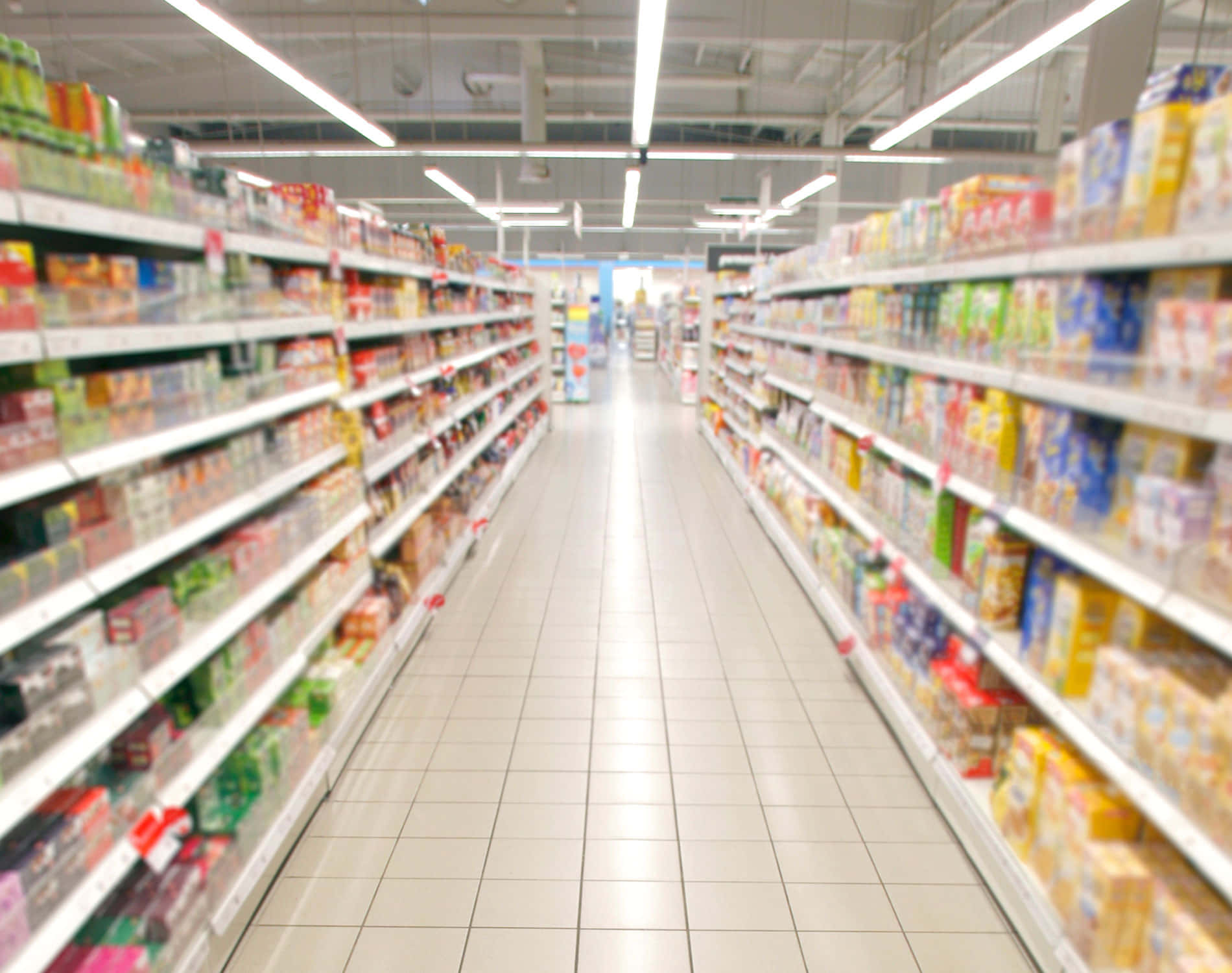 Grocery Store 桌布 壁紙 — 模糊的超級市場通道，明亮的螢光燈和貨架上色彩繽紛的產品盒。