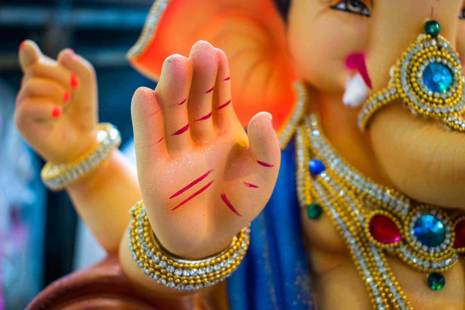 Vinayaka 桌布 壁紙 — 模糊背景前，色彩繽紛的象神雕像手部特寫，飾有紅色標記和金色珠寶。