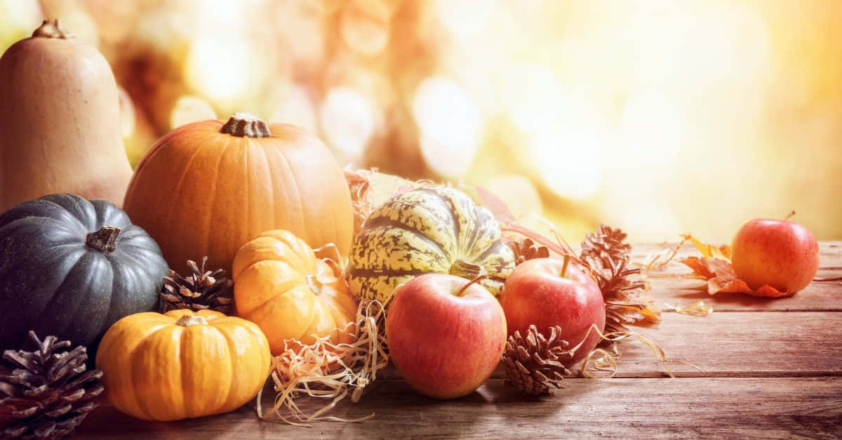Fall Thanksgiving 桌布 壁紙 — 樸實的秋季靜物畫，南瓜、蘋果和松果擺放在木桌上，背景是溫暖的金色散景。