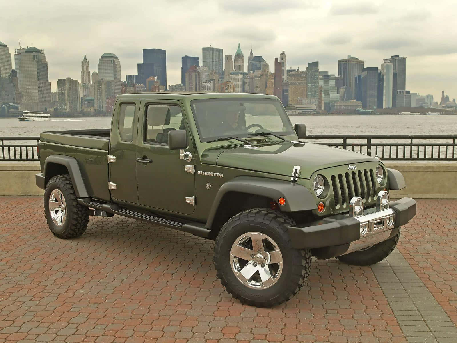 Jeep Gladiator 桌布 壁紙 — 橄欖綠色的Jeep Gladiator皮卡車停在磚砌路面上，背景是陰天下的紐約市天際線。