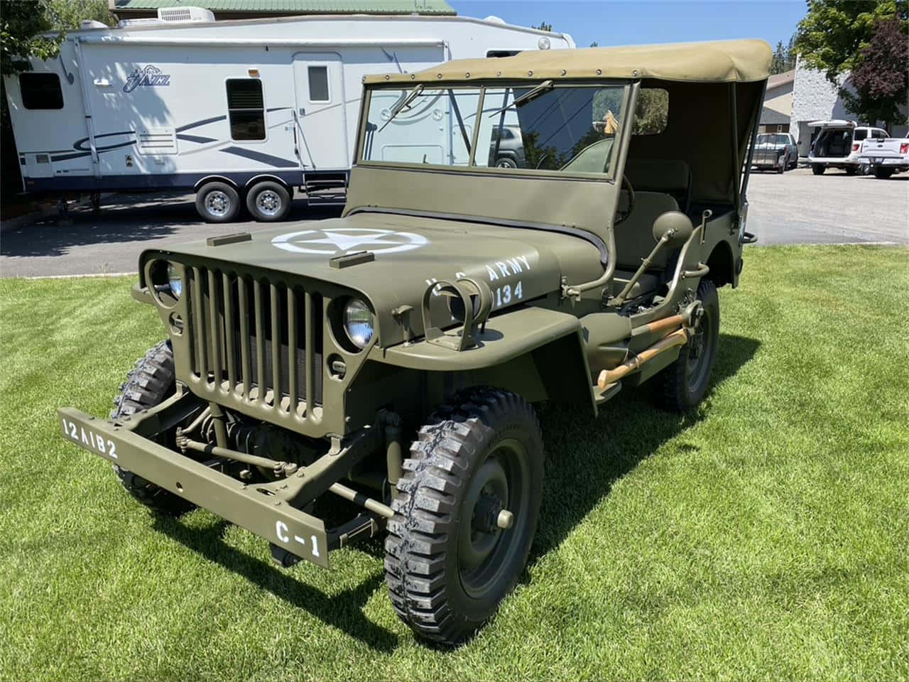 Jeep Willys 桌布 壁紙 — 橄欖綠軍用吉普車停放在鮮綠色草地上，晴朗天空下，背景有露營車。