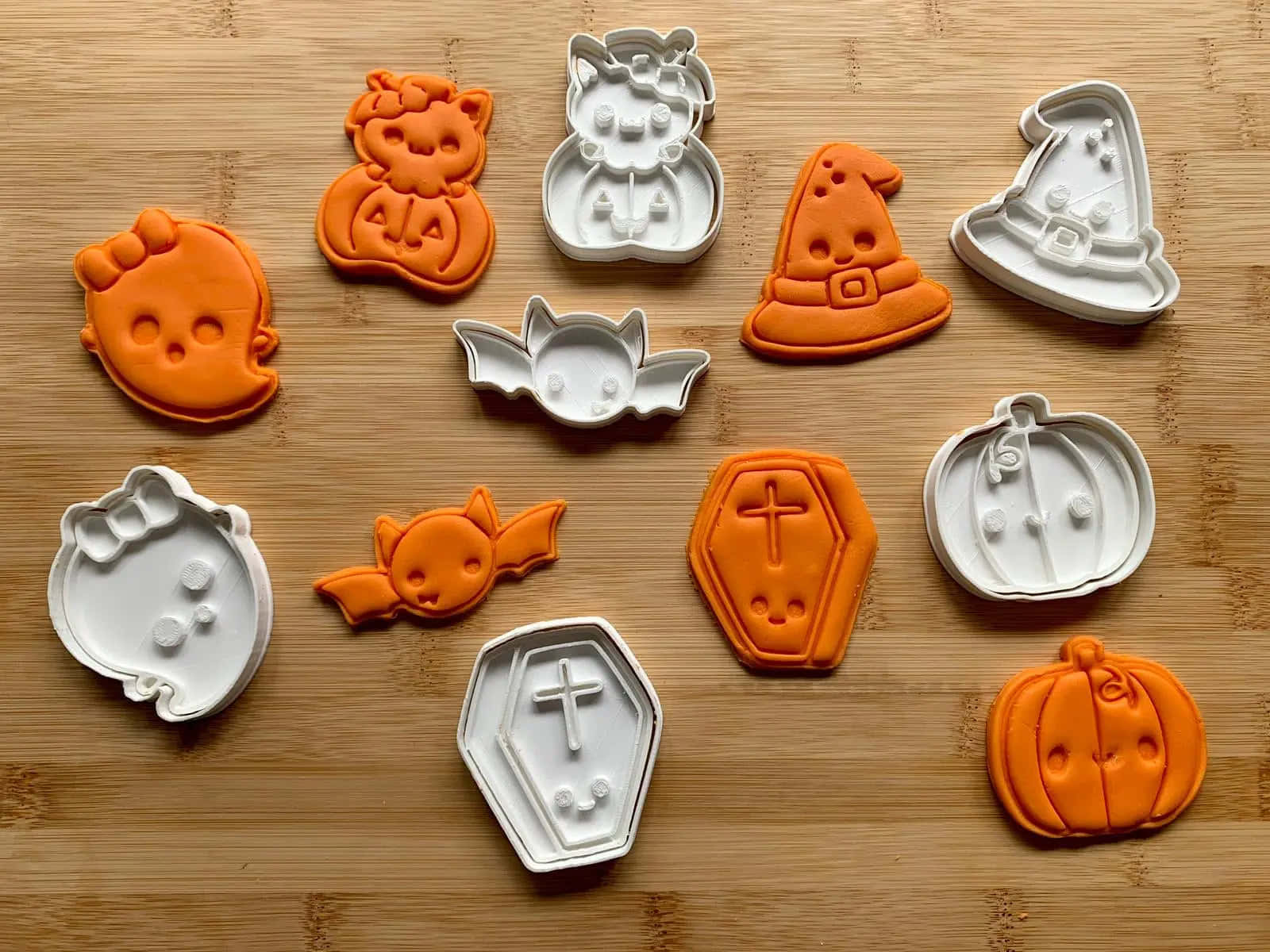 Halloween Cookie Cutters 桌布 壁紙 — 橘色和白色的萬聖節餅乾模具，形狀有南瓜、蝙蝠和棺材，排列在木質表面上。