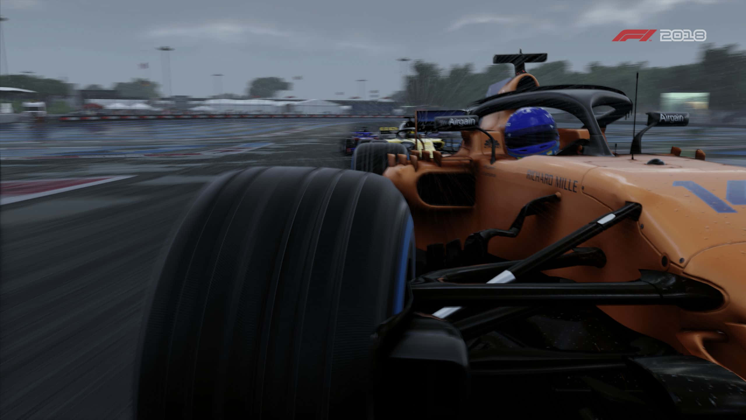 F1 2018 桌布 壁紙 — 橙色一級方程式賽車在潮濕賽道上疾馳的特寫，背景模糊，天色陰沉。
