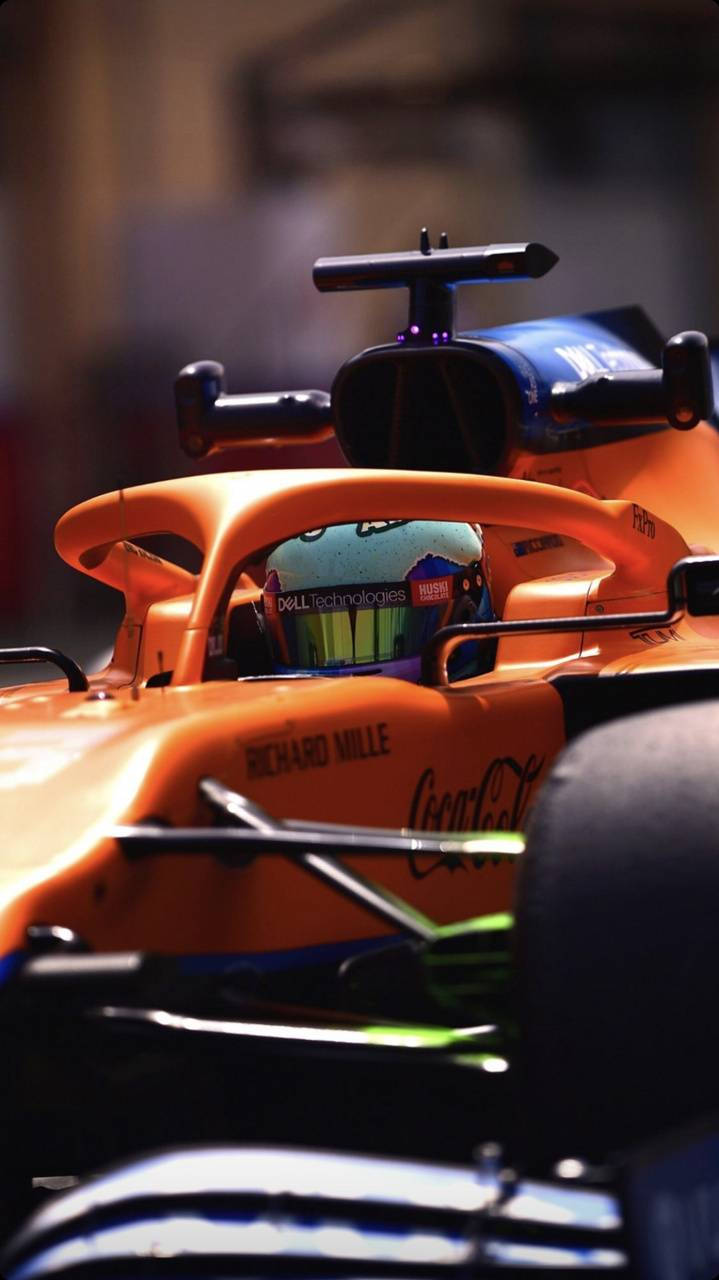 Racing 桌布 壁紙 — 橙色一級方程式賽車特寫，車手戴頭盔在駕駛艙內，處於明亮燈光下。