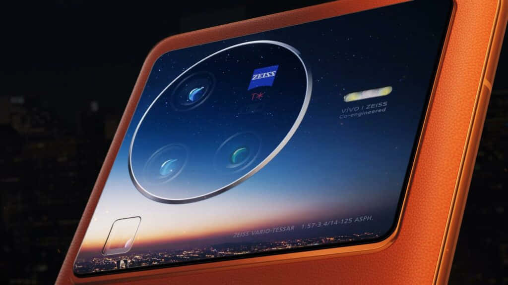 Device 桌布 壁紙 — 橙色智慧型手機的特寫，圓形相機模組顯示日落城市景觀和 Zeiss 品牌標誌。