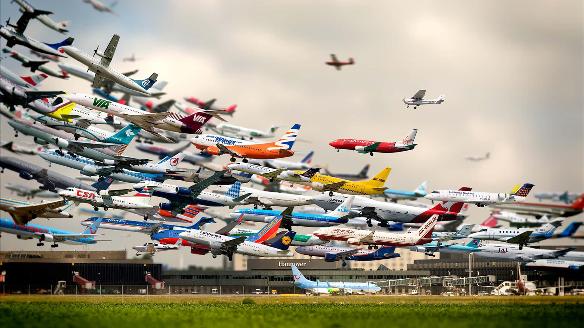 飛機 桌布 壁紙 — 機場上空多雲的天空背景下，各種飛行階段的彩色商用飛機密集群。