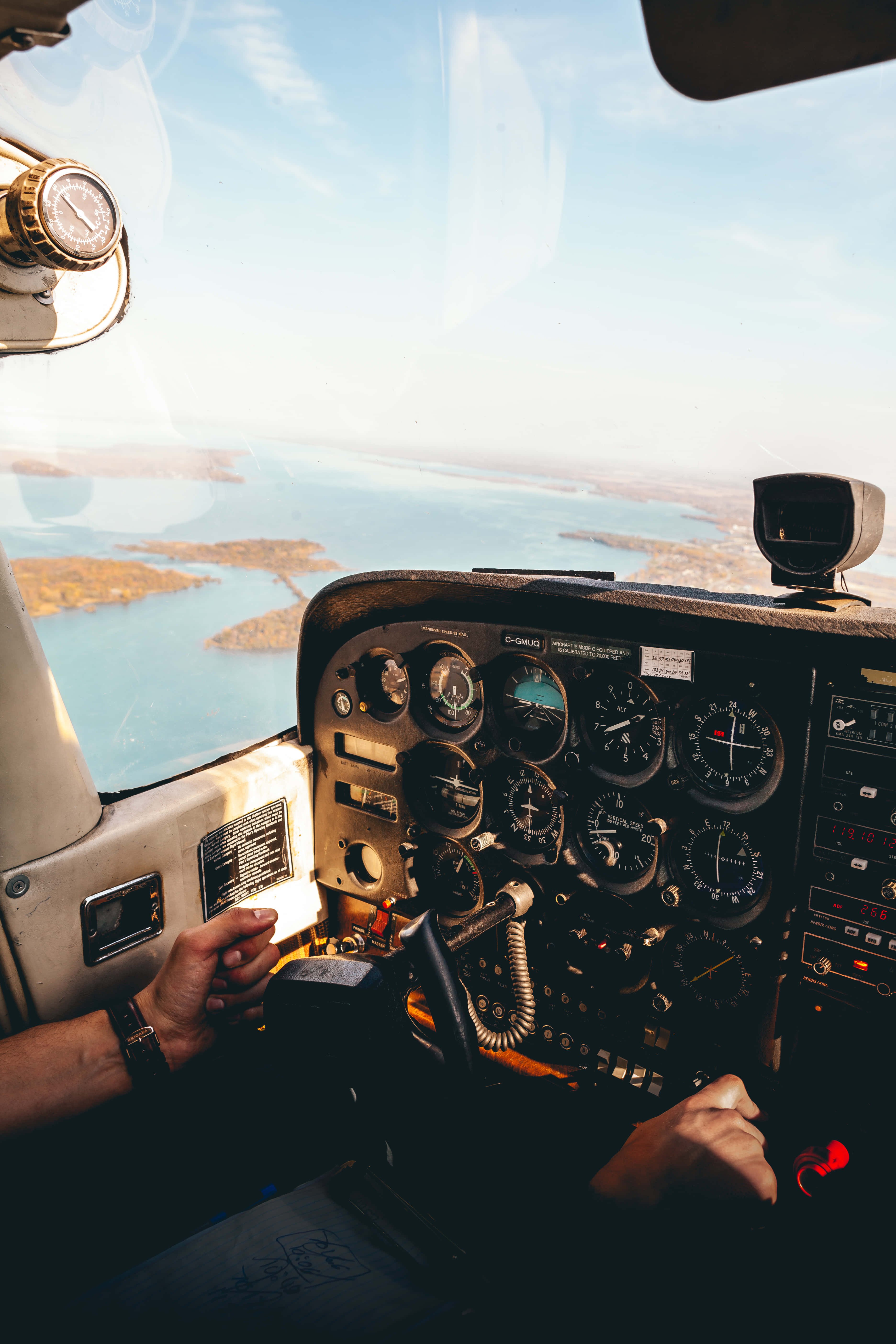 Plane 桌布 壁紙 — 機師雙手緊握小型飛機駕駛艙內的操控裝置，俯瞰陽光普照的海岸景觀，碧綠海水與島嶼盡收眼底。