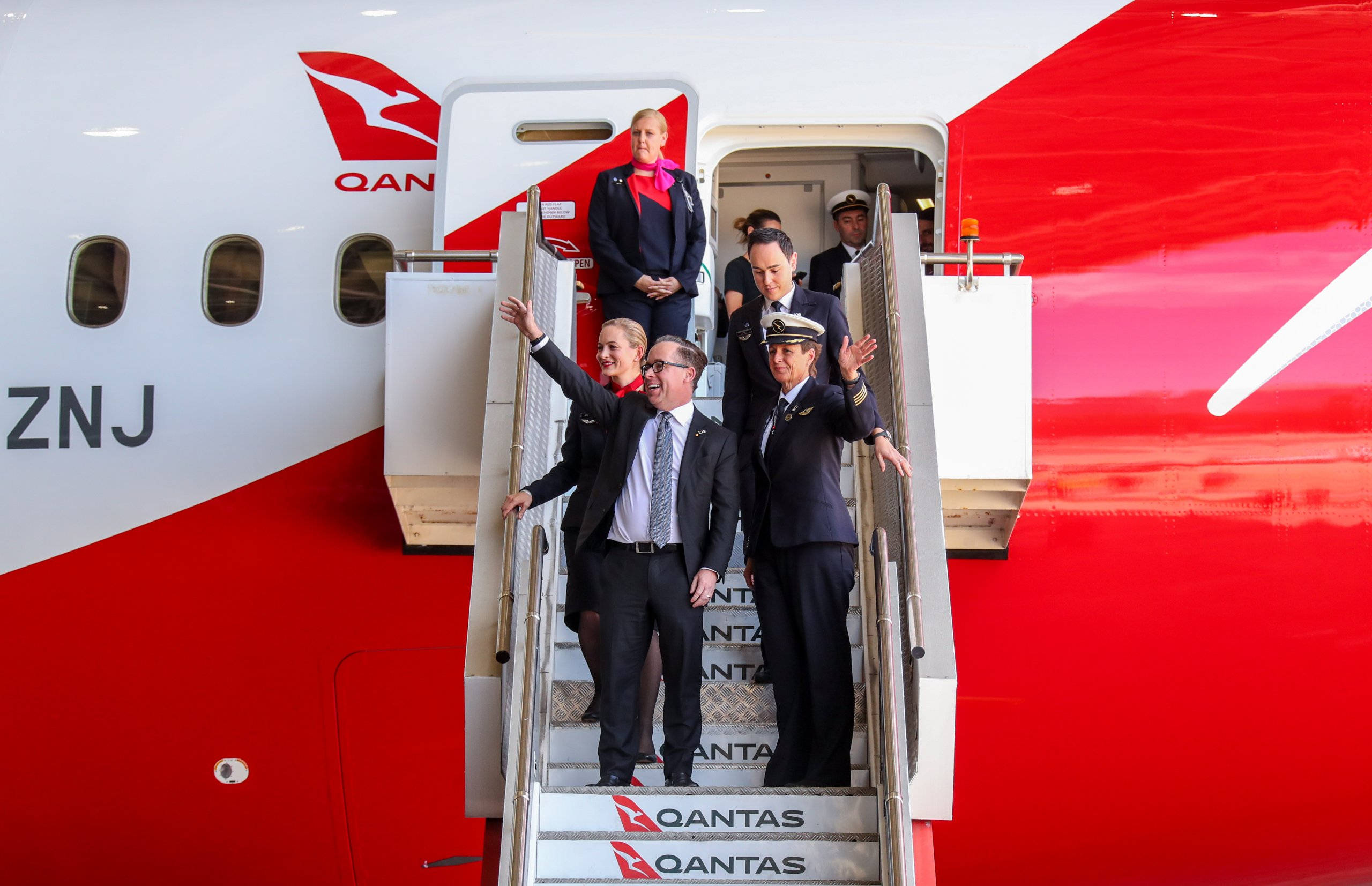 Plane 桌布 壁紙 — 機組人員和乘客走下紅白相間的澳洲航空飛機的樓梯，向登機口的圍觀者揮手。