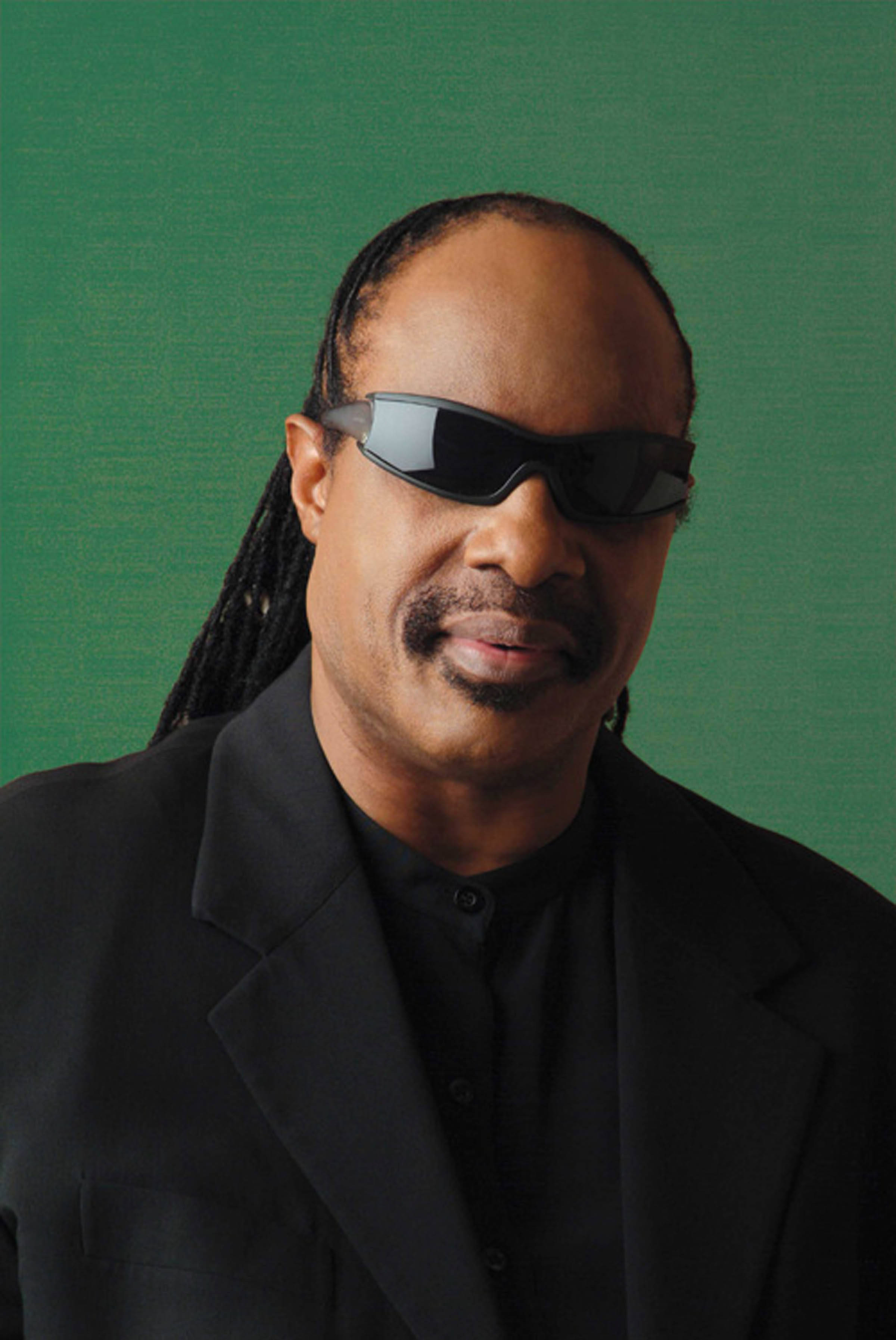音樂 桌布 壁紙 — 歌手Stevie Wonder戴上黑色太陽眼鏡和西裝，在純綠色背景前展現自信表情。