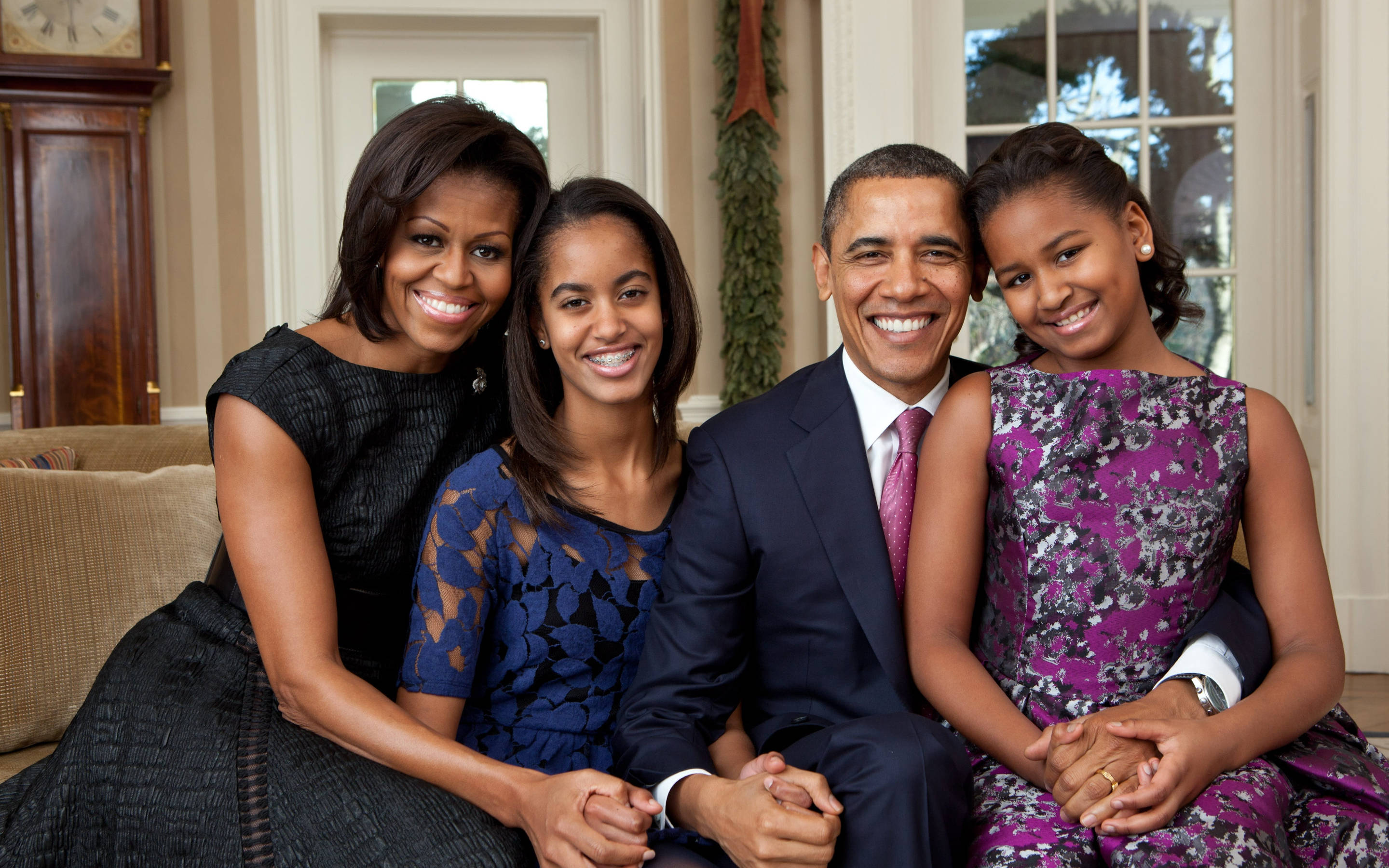 Barack 桌布 壁紙 — 歐巴馬一家在陽光充足的正式客廳中，坐在木製家具和綠色植物旁，溫暖地微笑。