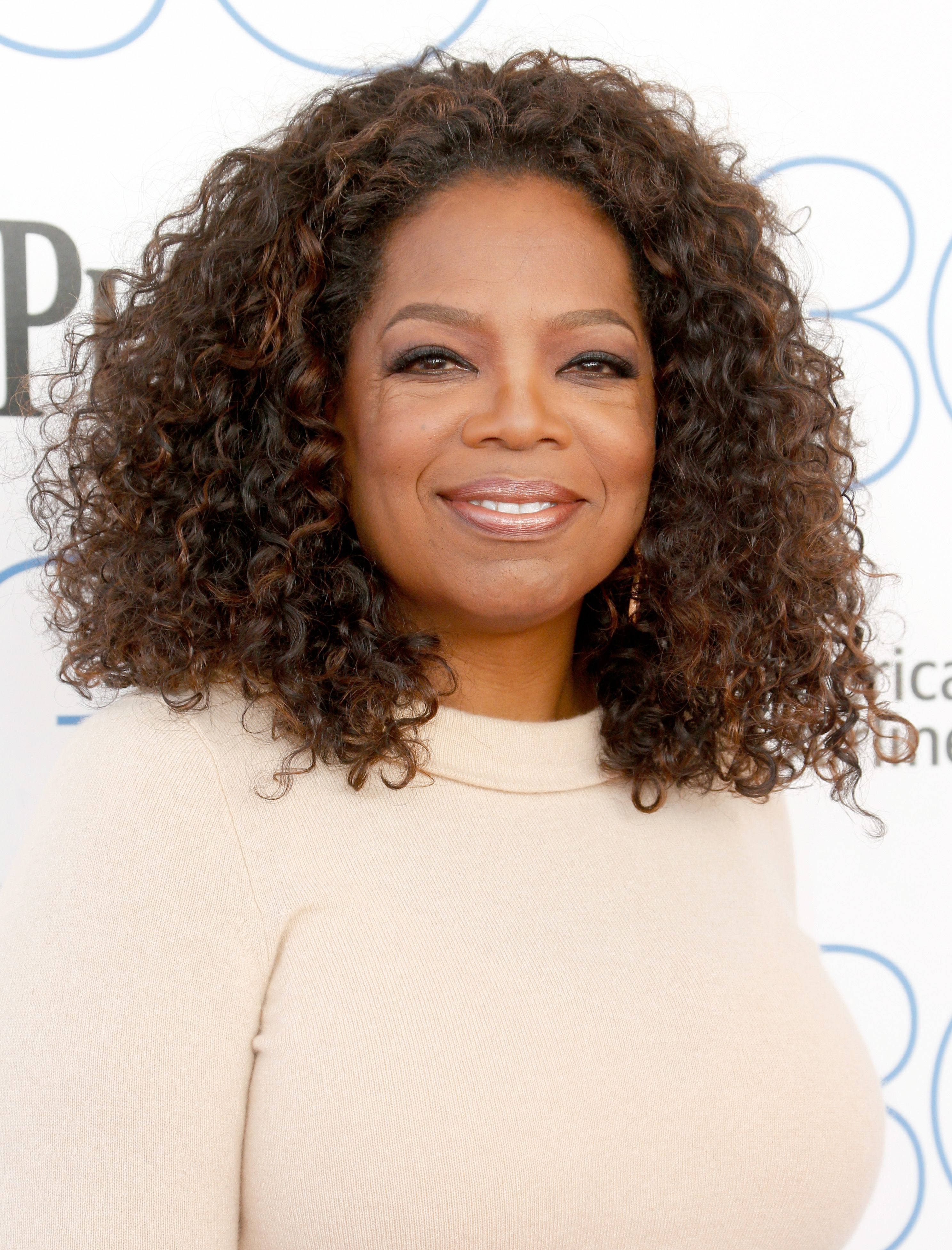 Oprah 桌布 壁紙 — 歐普拉·溫芙蕾在品牌活動背景前，以一頭豐盈捲髮溫暖地微笑。