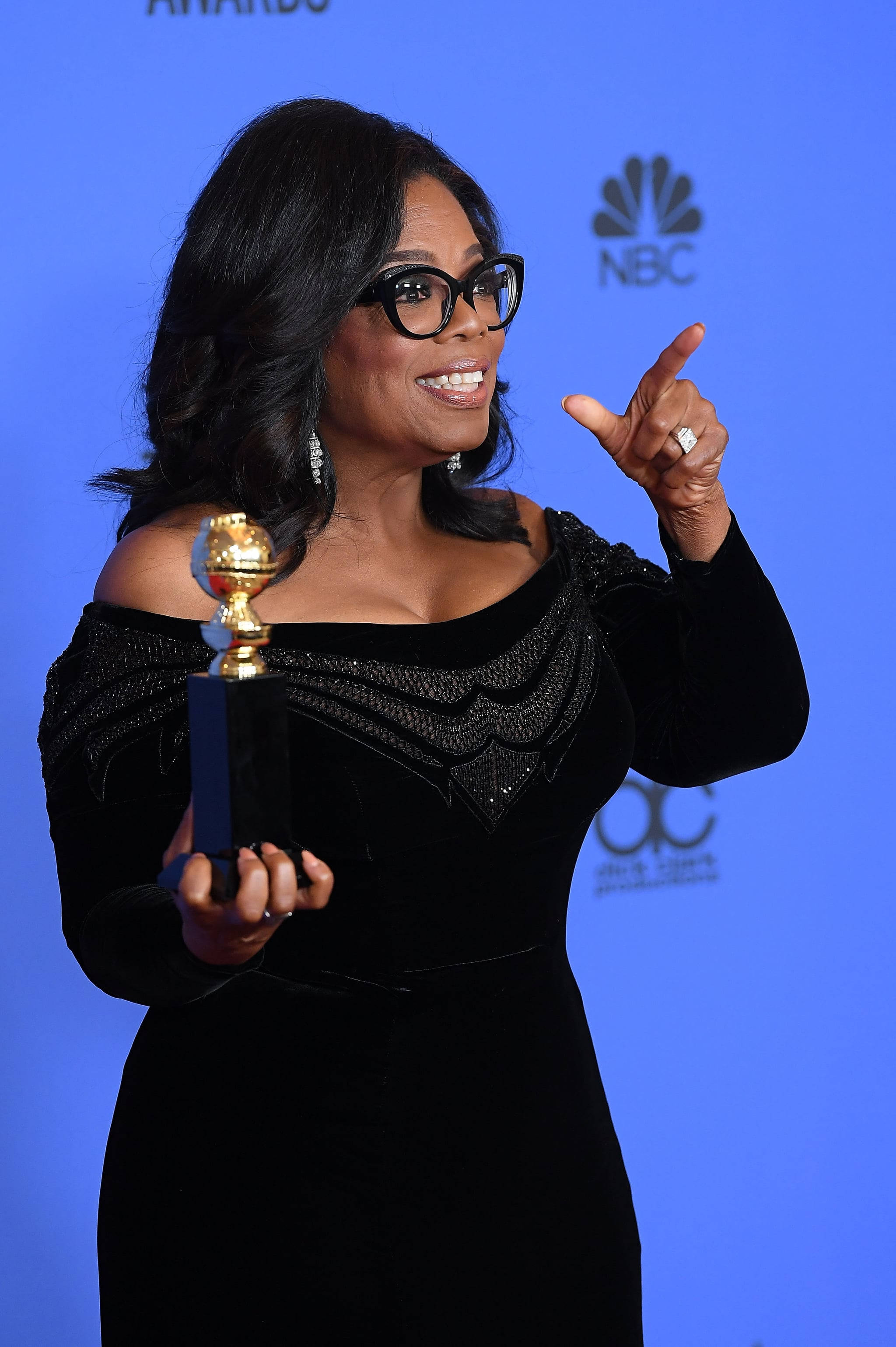Oprah 桌布 壁紙 — 歐普拉·溫芙蕾手持金球獎，另一隻手做手勢，在藍色活動背景前笑容滿面。