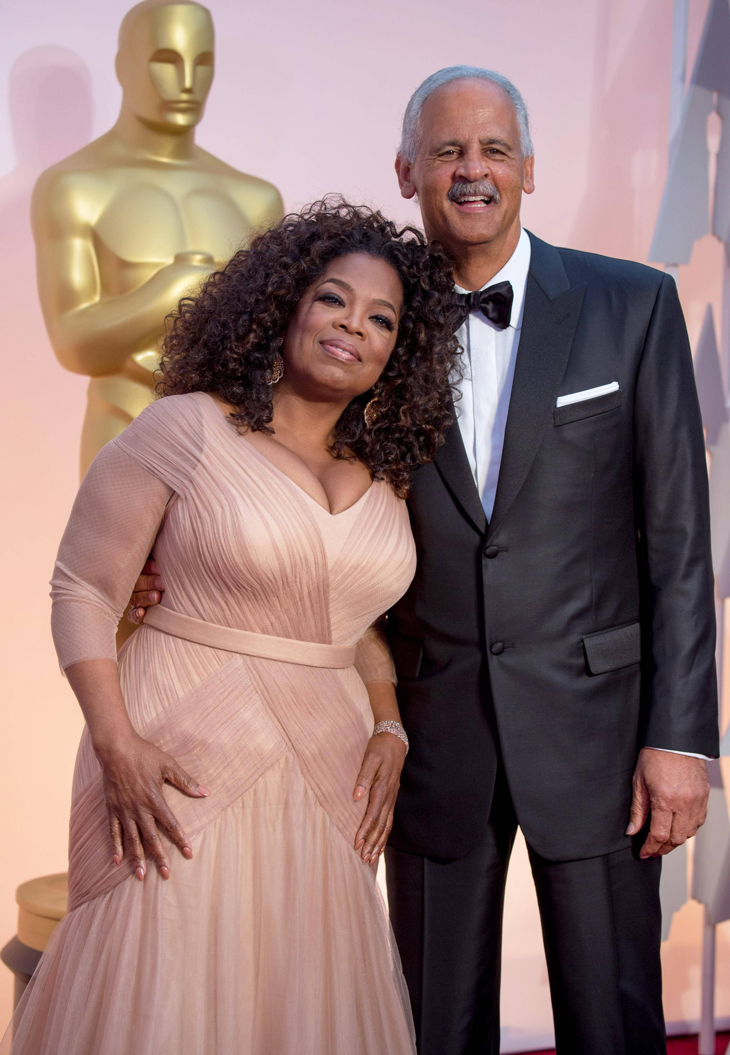 Oprah 桌布 壁紙 — 歐普拉·溫芙蕾與她的伴侶在明亮的活動燈光下，優雅地站在金色奧斯卡獎座旁邊的紅地毯上。