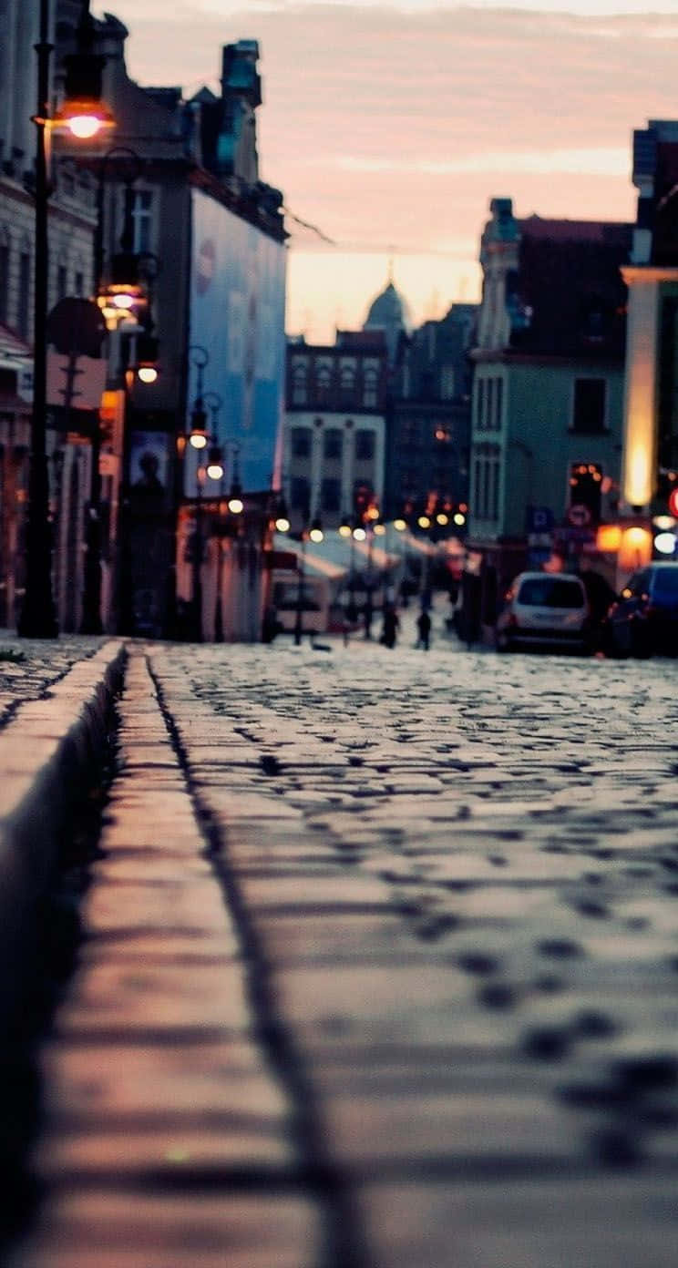 Road 桌布 壁紙 — 歐洲城市的鵝卵石街道在黃昏時分溫暖地發光，帶有模糊的路燈和柔和粉彩色的歷史建築。