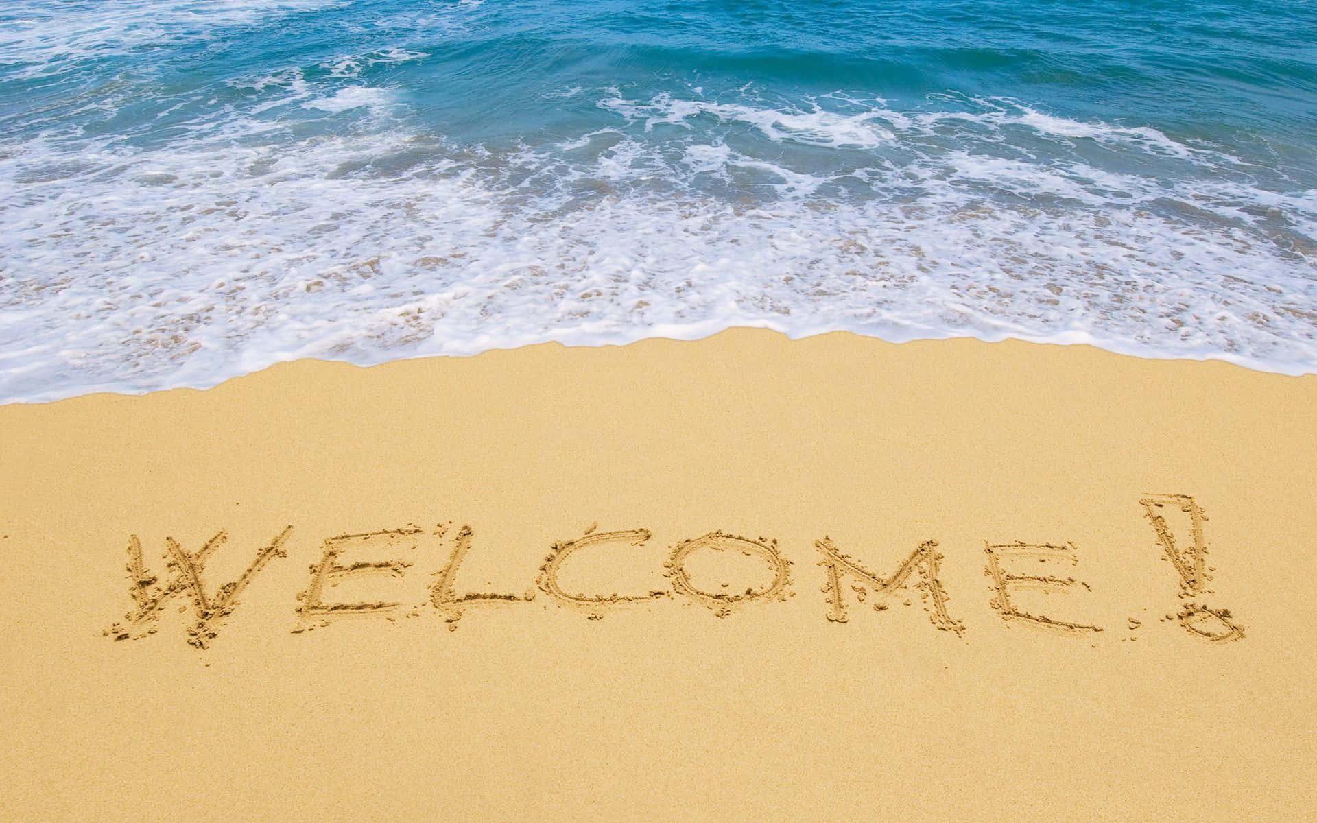 Welcome 桌布 壁紙 — 「歡迎」一詞寫在綠松色海浪邊緣的沙灘上。
