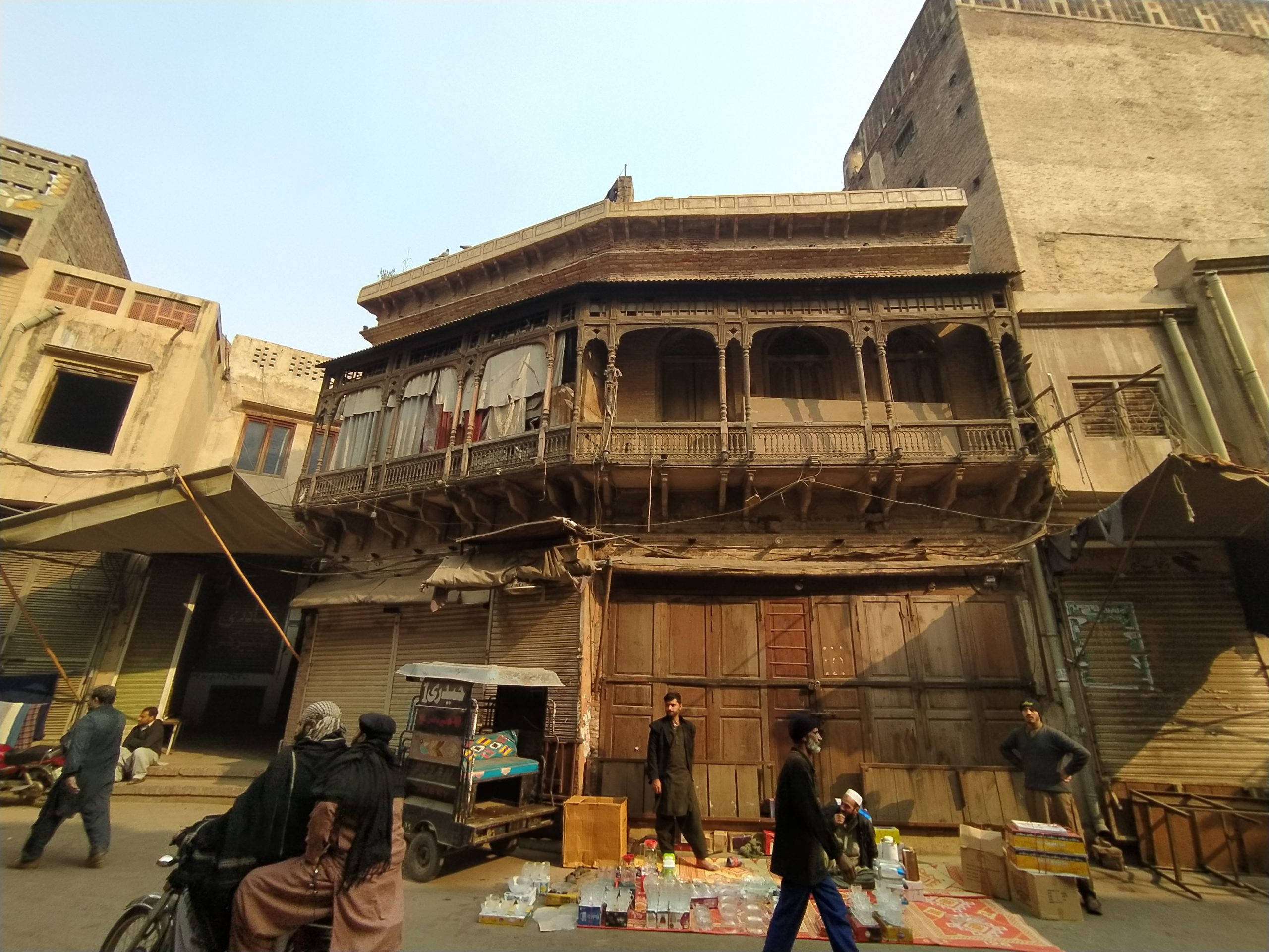 Lahore 桌布 壁紙 — 歷史城區的繁華街景，人們走過一棟帶陽台的風化木建築。