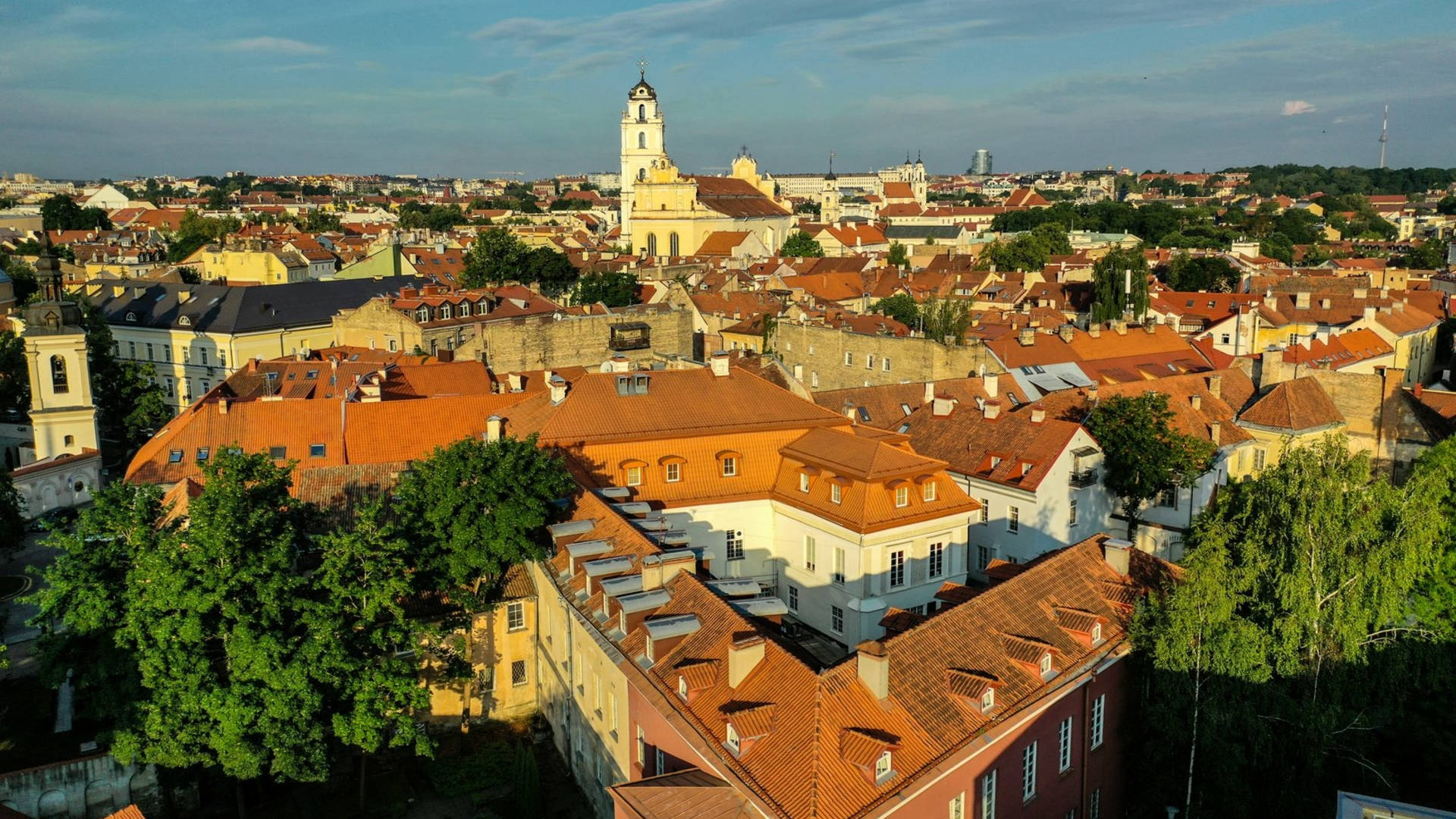 Vilnius 桌布 壁紙 — 歷史城市景觀的鳥瞰圖，擁有陶土屋頂和教堂塔樓，沐浴在金色日落光芒中。