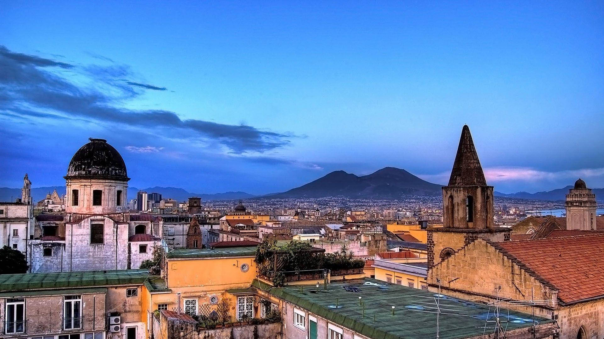 Naples 桌布 壁紙 — 歷史城市景觀的黃昏全景，擁有圓頂教堂和陶土屋頂，深藍色天空下遠山連綿。