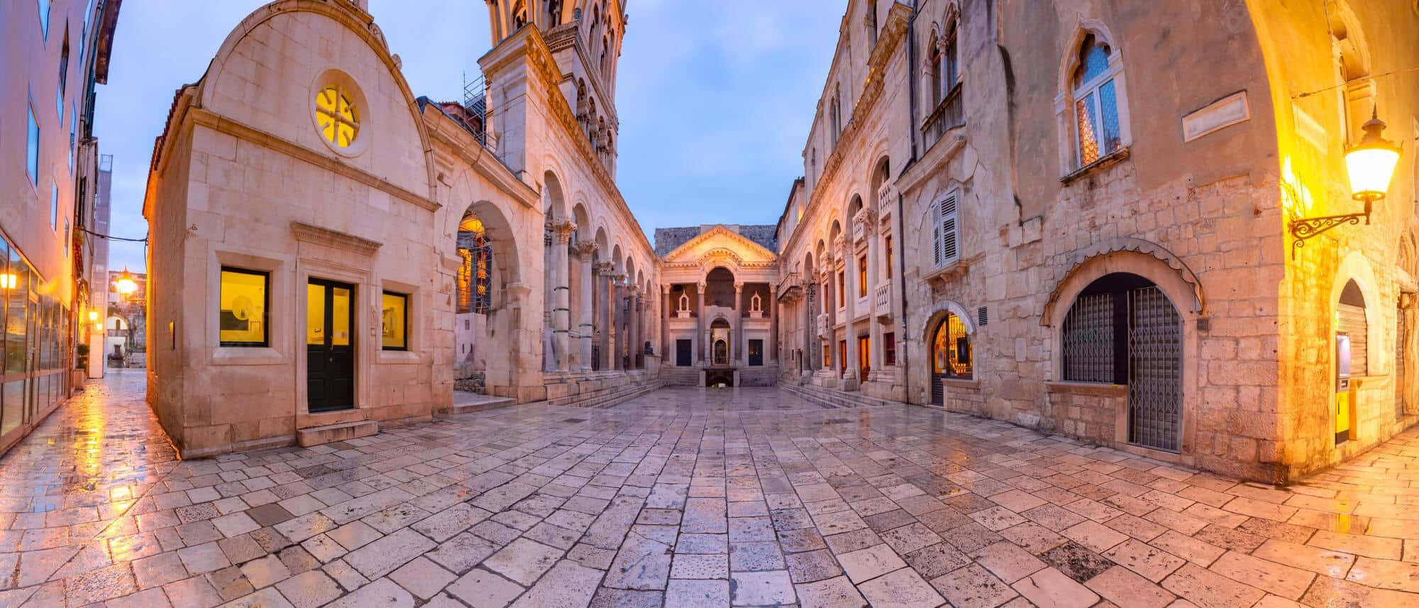 Croatia 桌布 壁紙 — 歷史建築之間濕漉漉的石頭庭院，在暮色中的街燈和窗戶燈光下溫暖地發光。